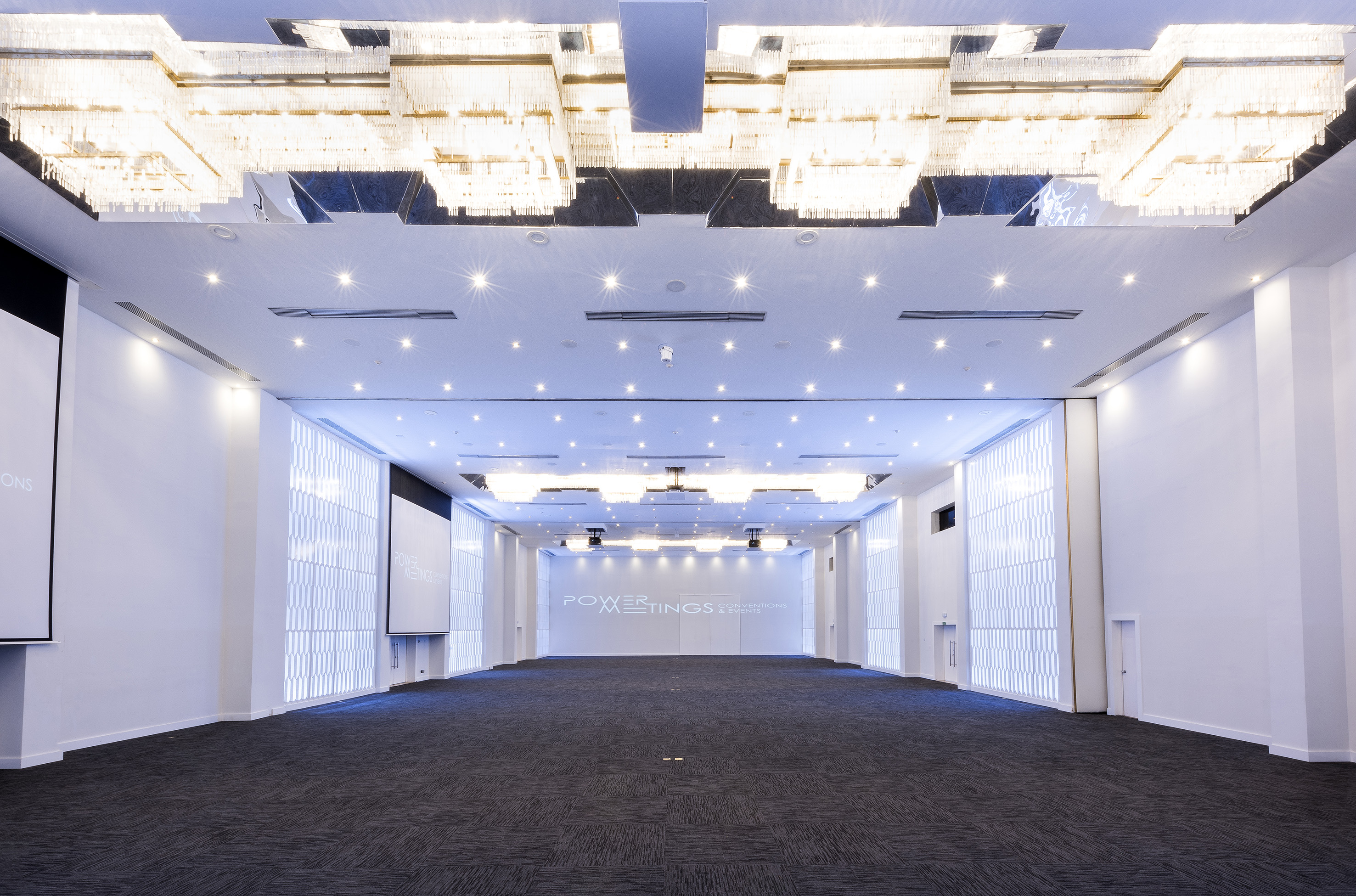 Modern conference hall with chandeliers and 'POWER MEETINGS' display.
