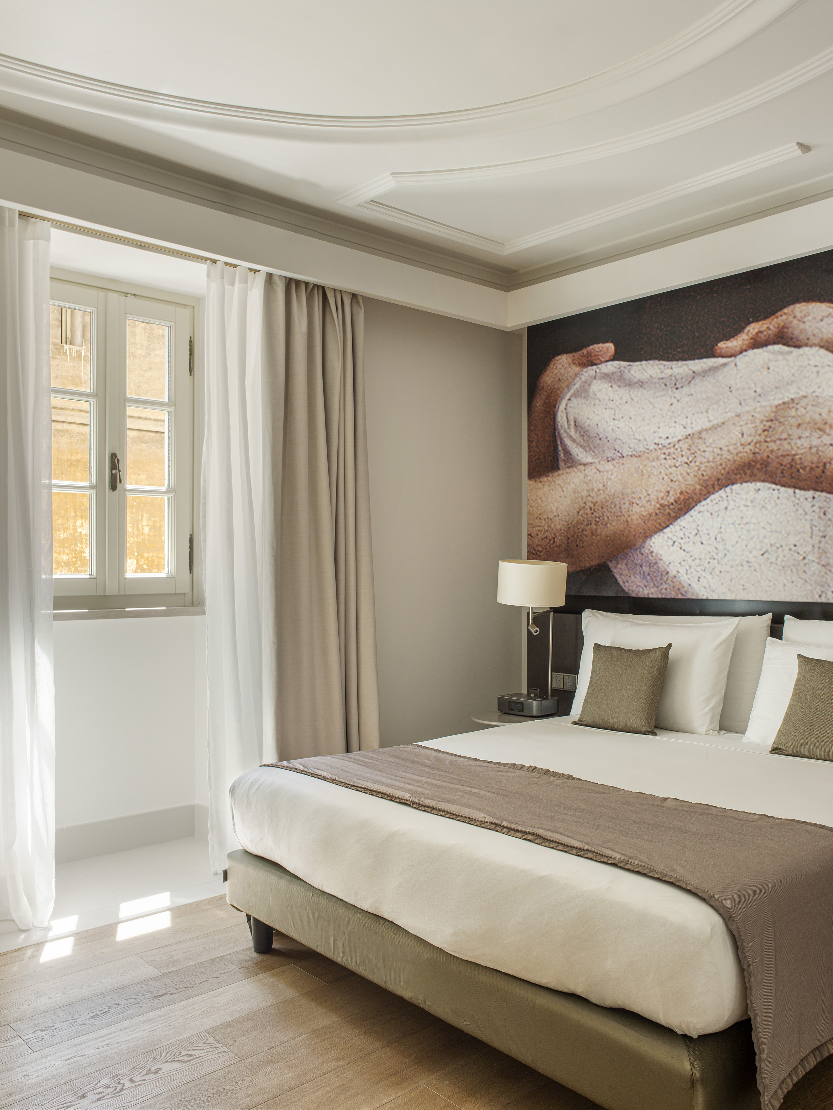 Modern hotel bedroom with white bed, large wall art, and sunlit window.