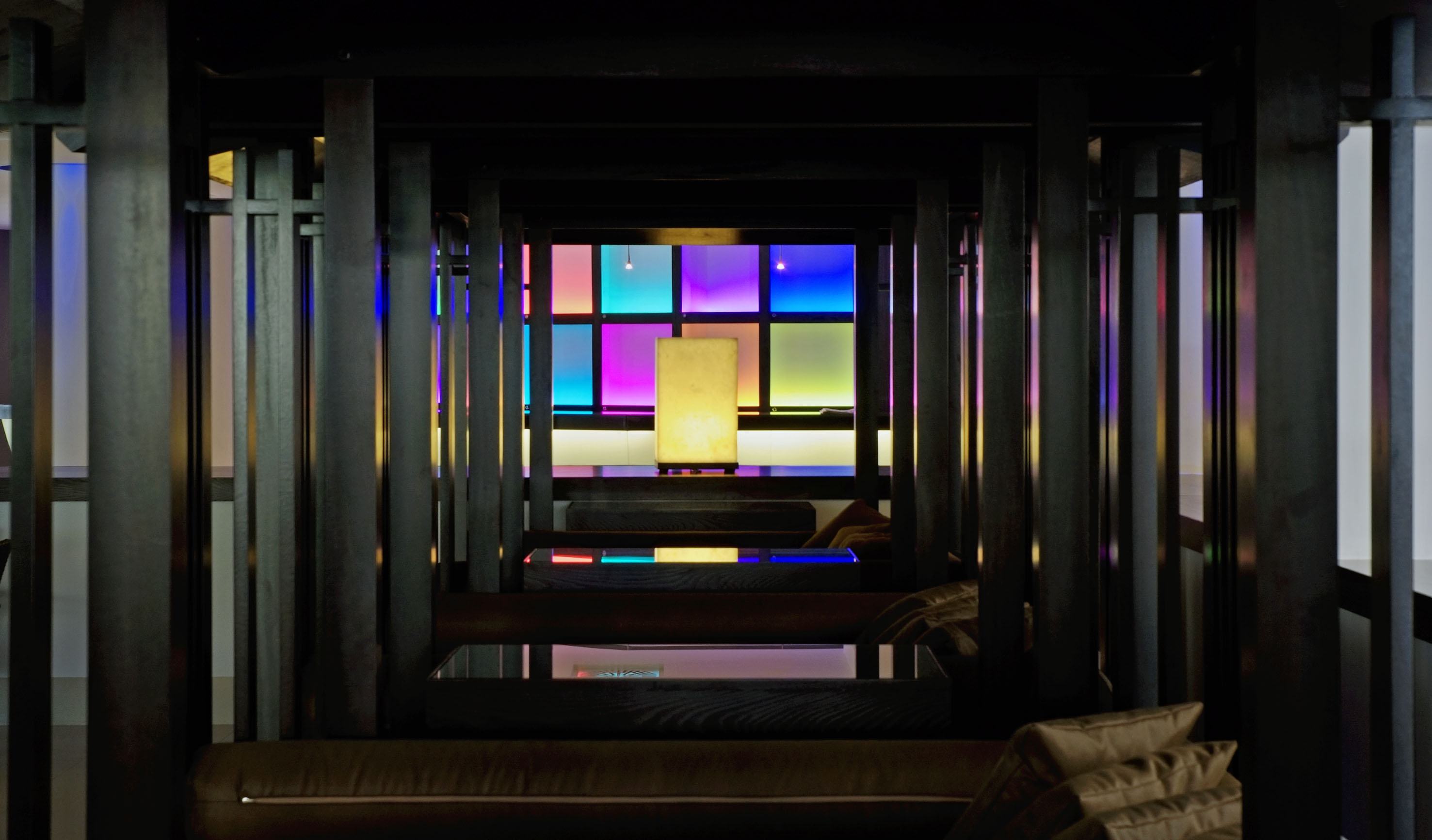Dark modern lounge with wooden beams, colorful glowing grid wall, and central lamp.