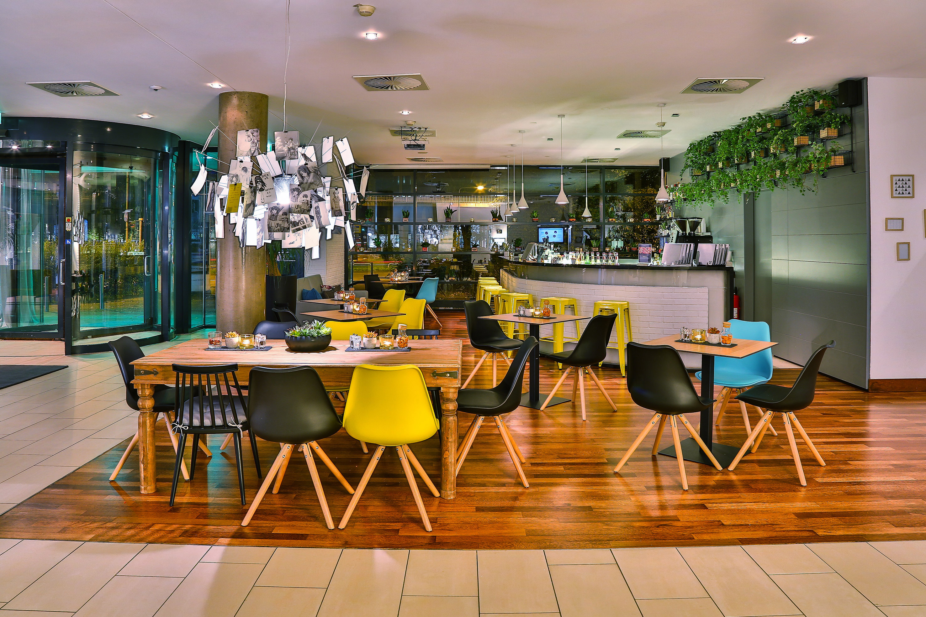 Modern restaurant bar with colorful seating, wooden floor, and photo chandelier.