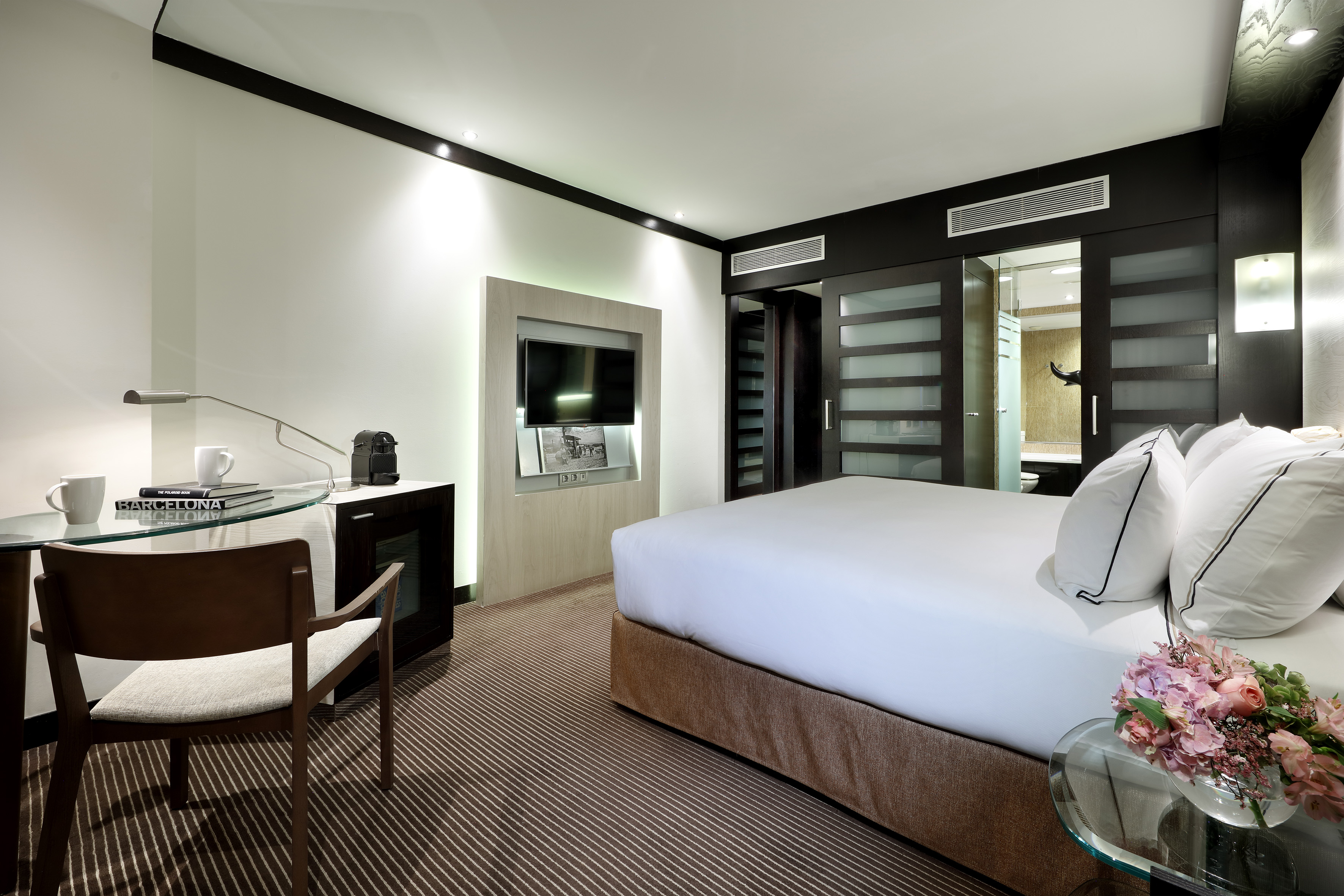 Modern hotel room with king bed, work desk, TV, and ensuite bathroom access.