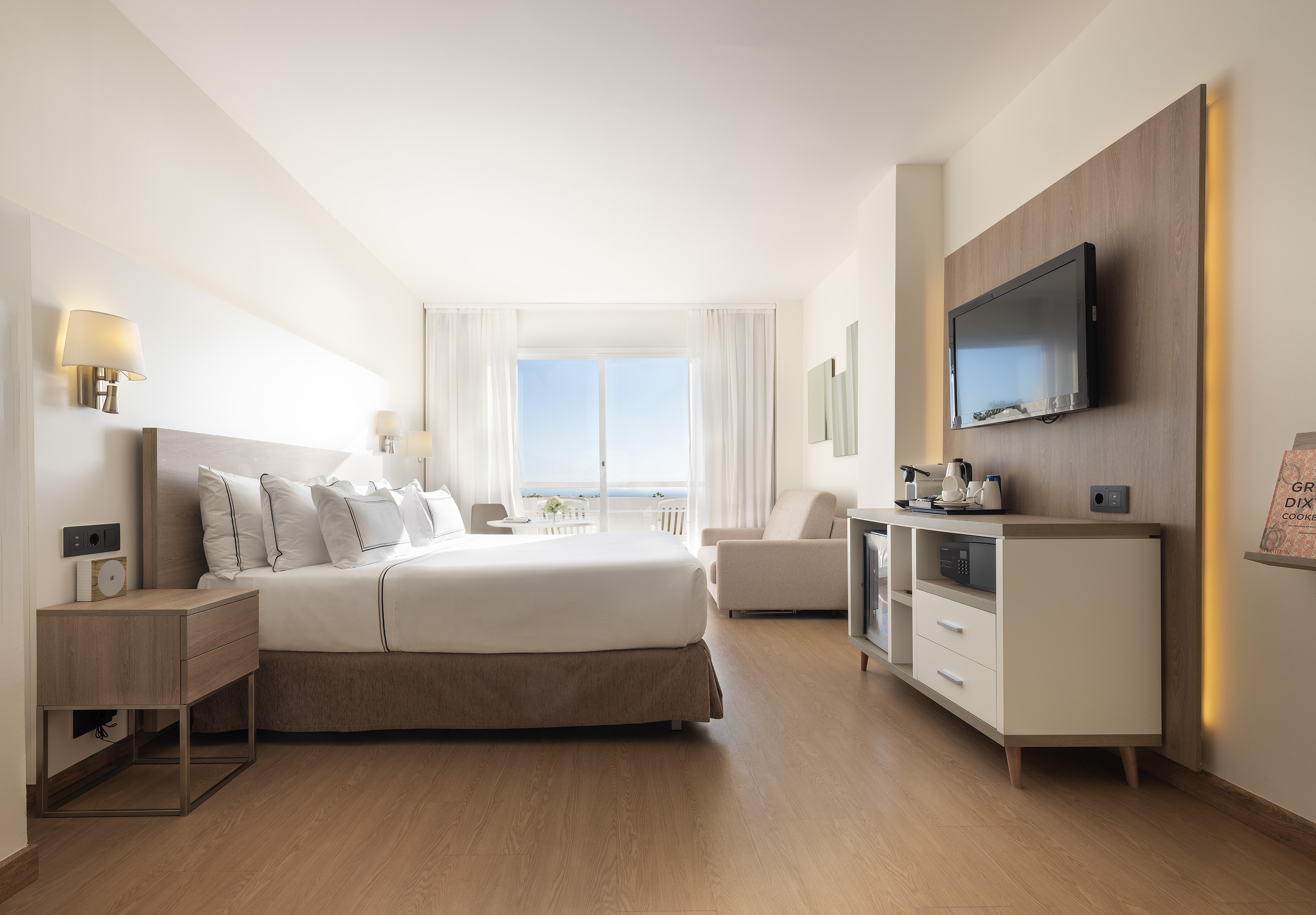Modern hotel room with ocean view balcony, king bed, and TV.