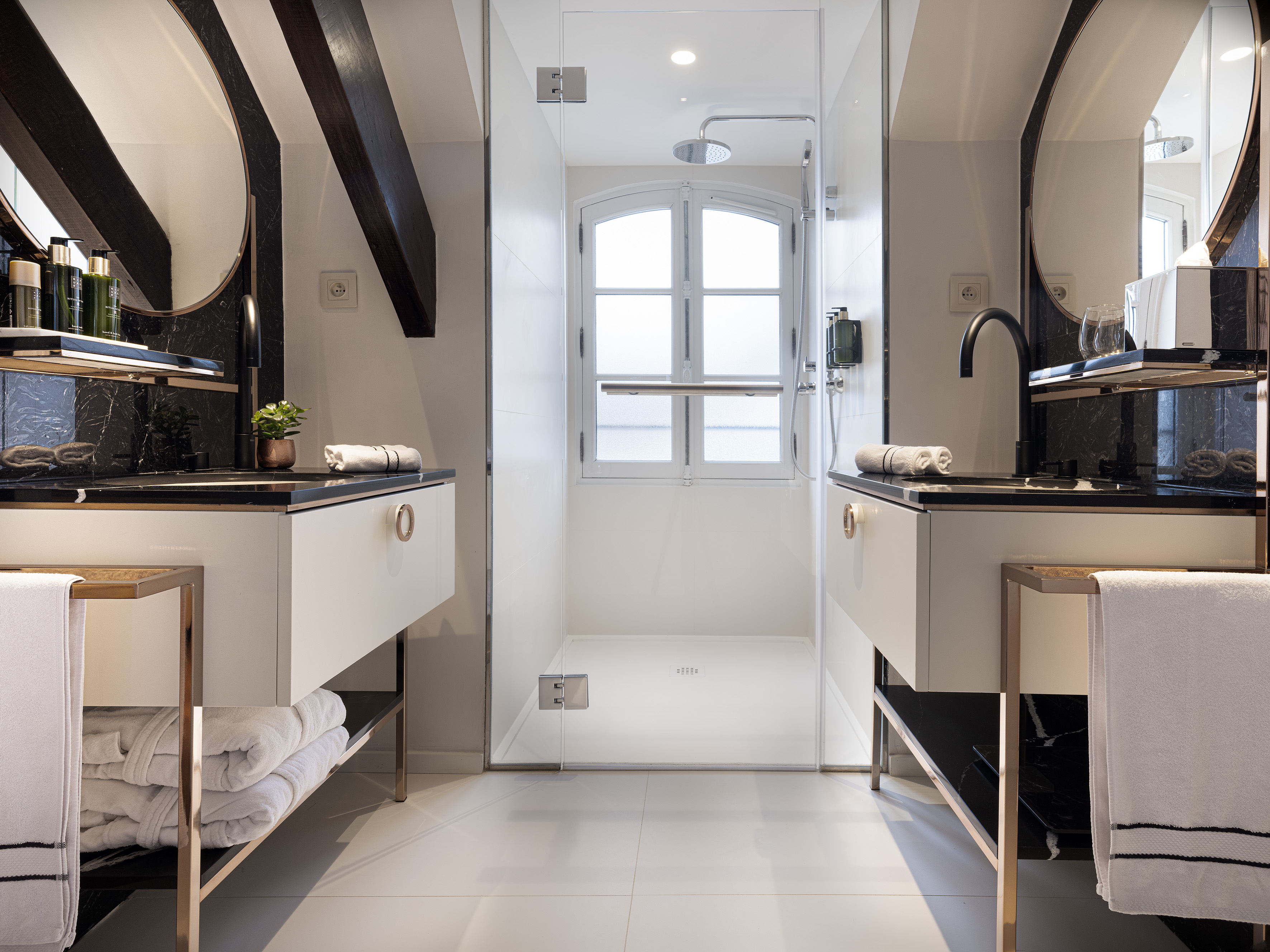 Stylish bathroom with twin black marble vanities, round mirrors, and walk-in shower.