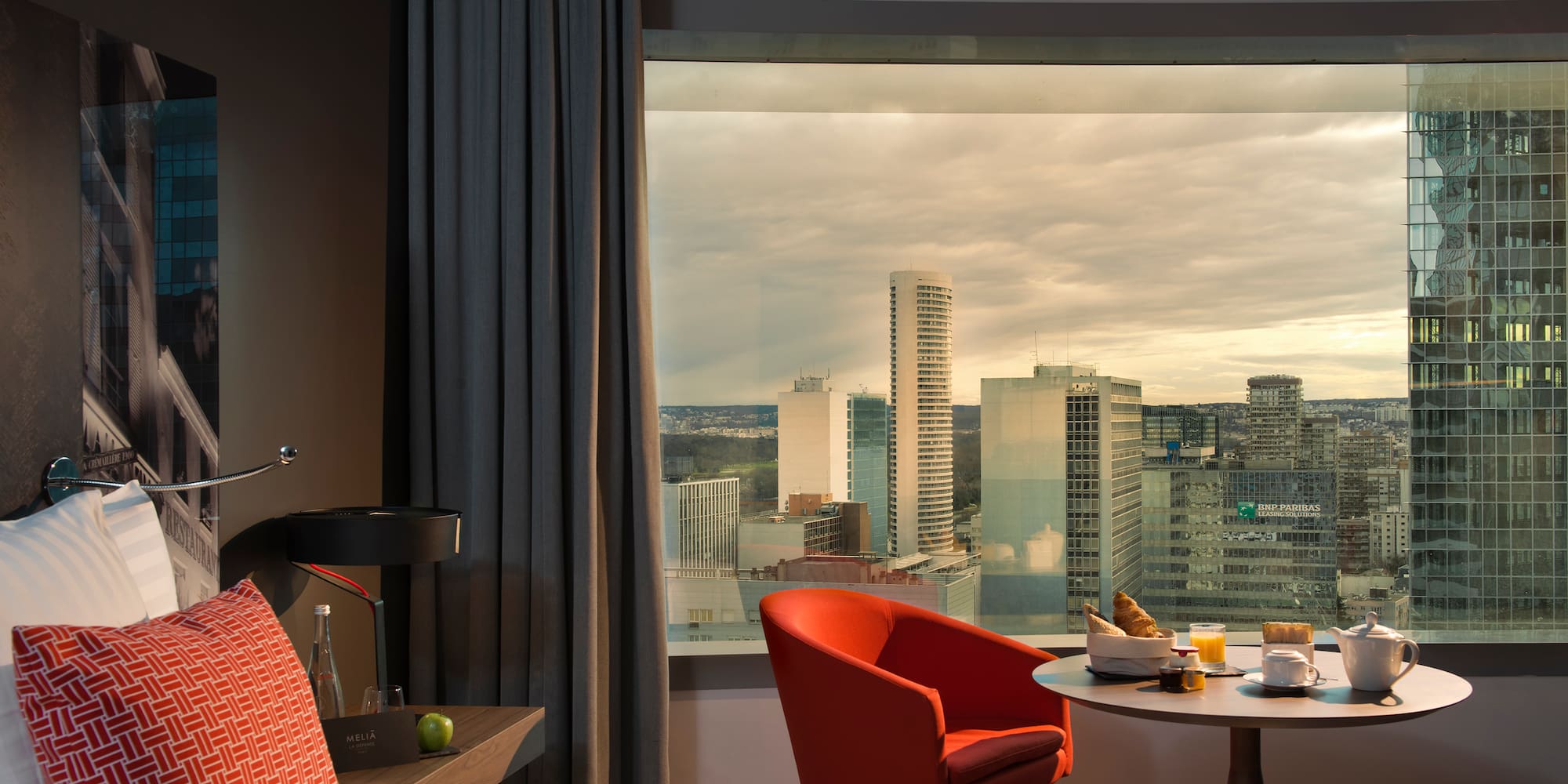 a room with a window and a bed and a table with food and a city view
