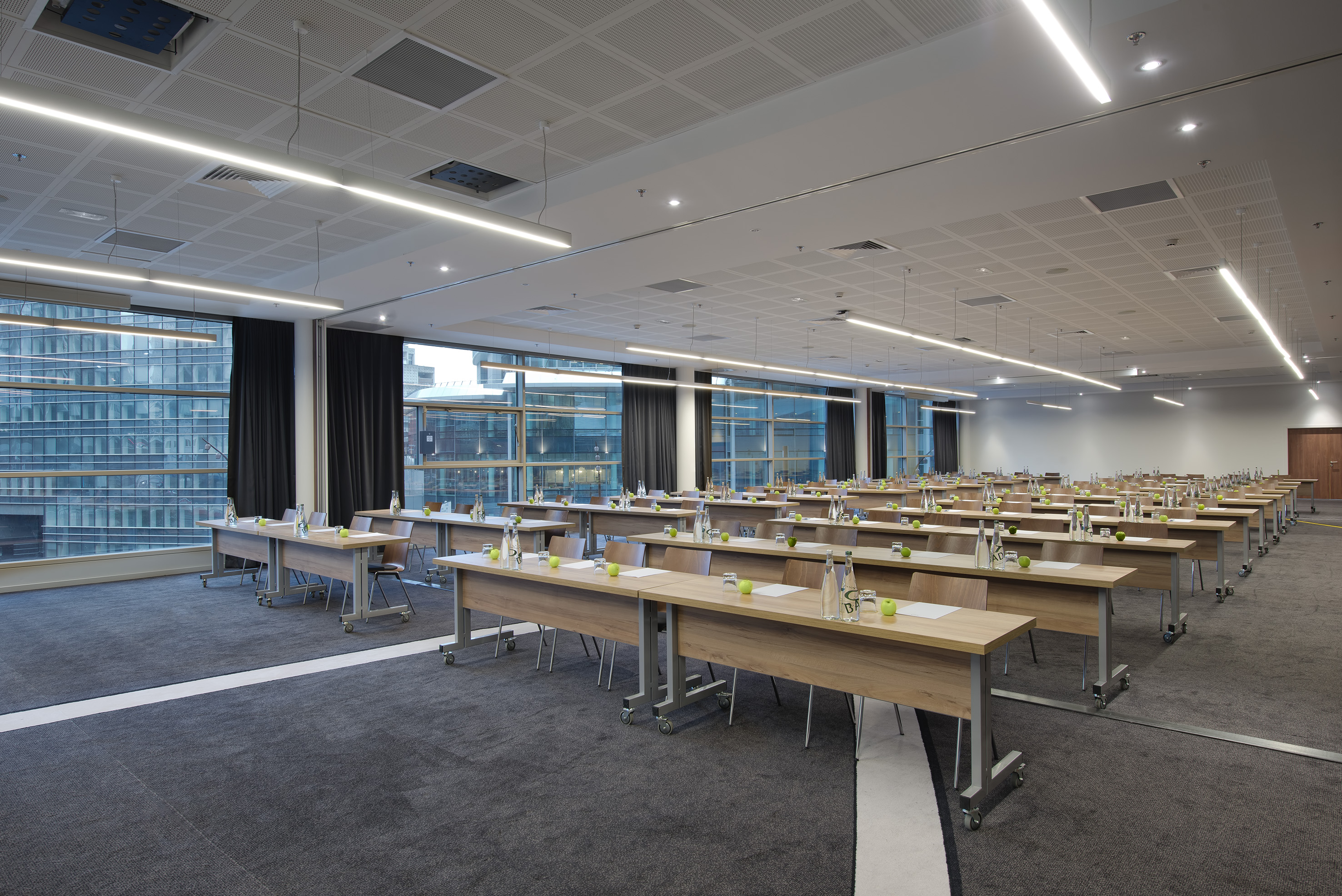 Corporate meeting room setup with tables, chairs, water bottles, and city views.