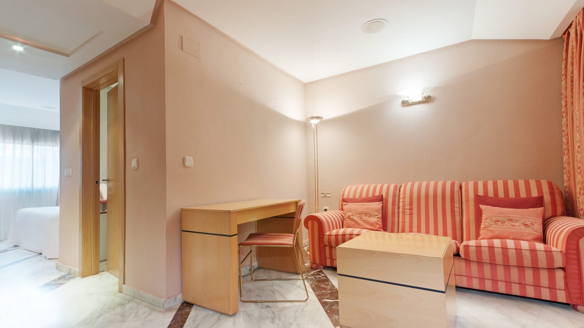 Hotel suite living room with orange striped sofa, wooden desk, and marble floor.
