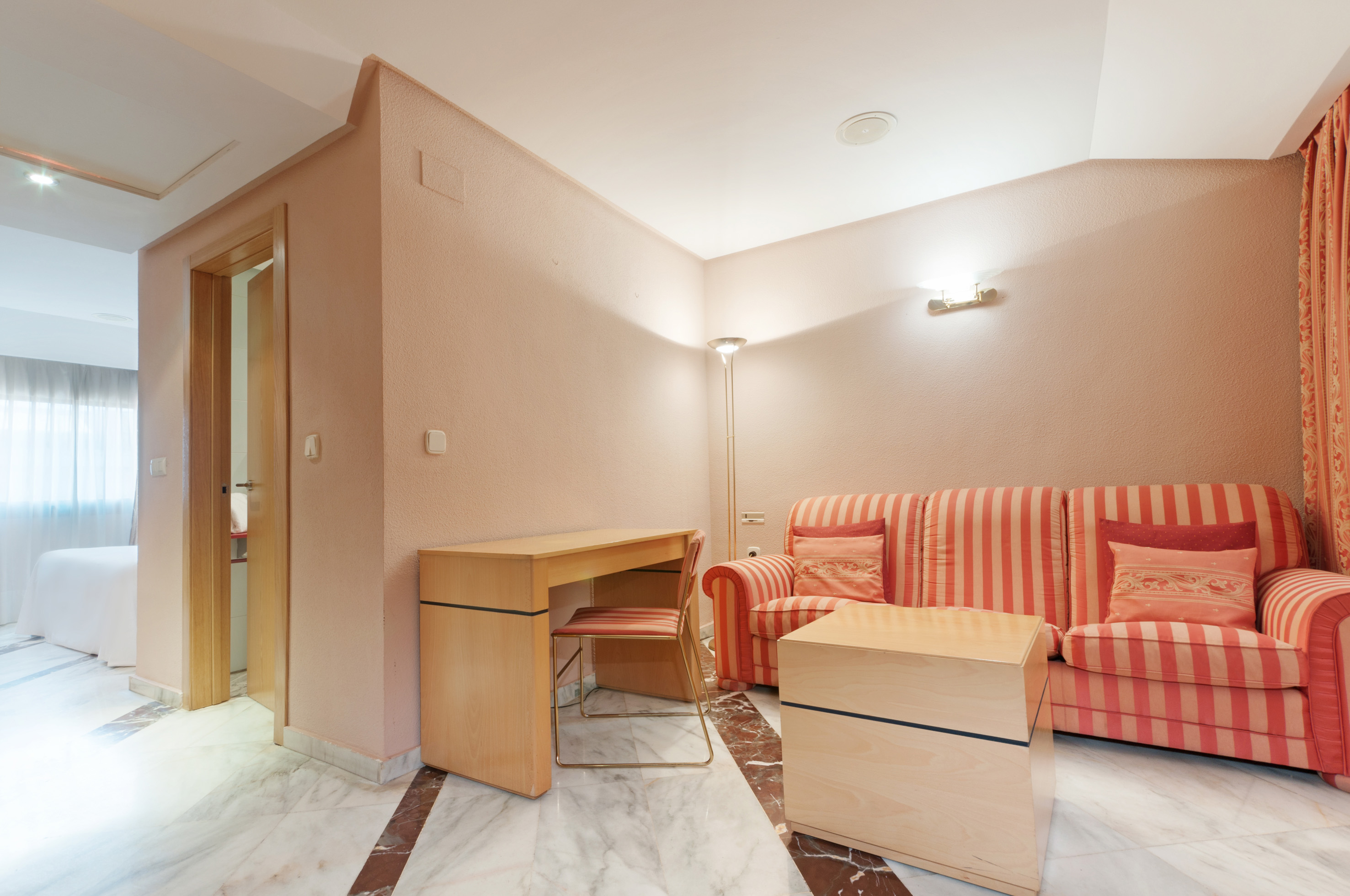 Hotel suite living room with orange striped sofa, wooden desk, and marble floor.