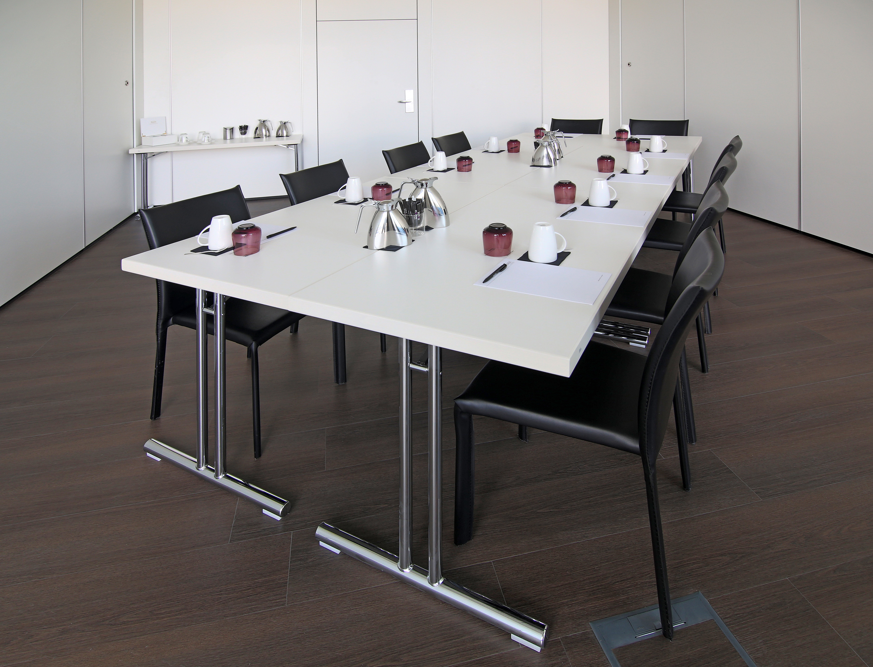Modern conference room with long white table, black chairs, and coffee service.