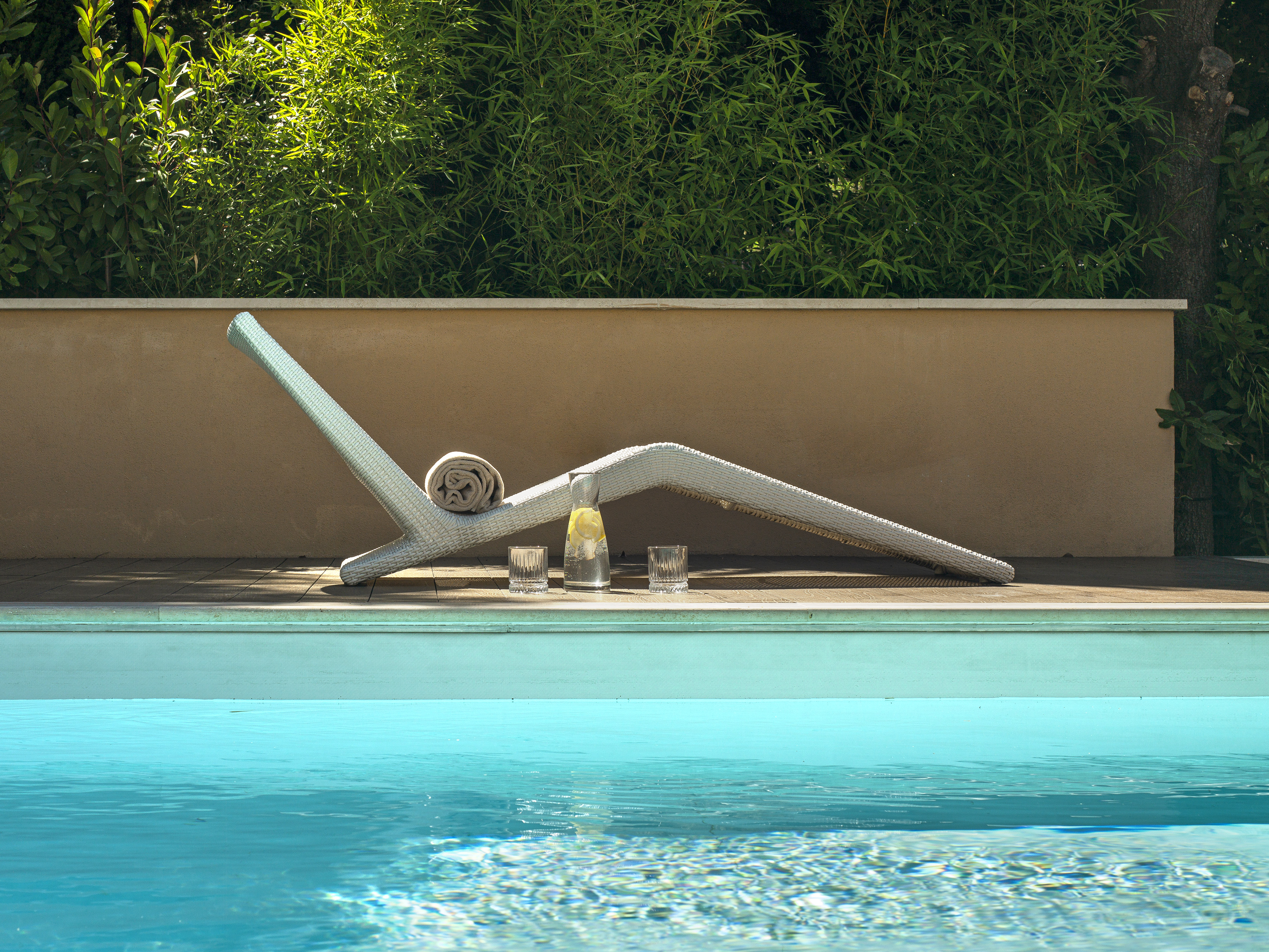 White lounge chair, lemonade by a blue pool, green foliage backdrop.