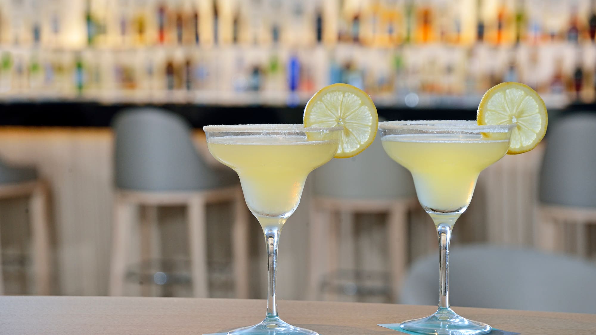 two glasses of yellow liquid with lemon slices on top of them