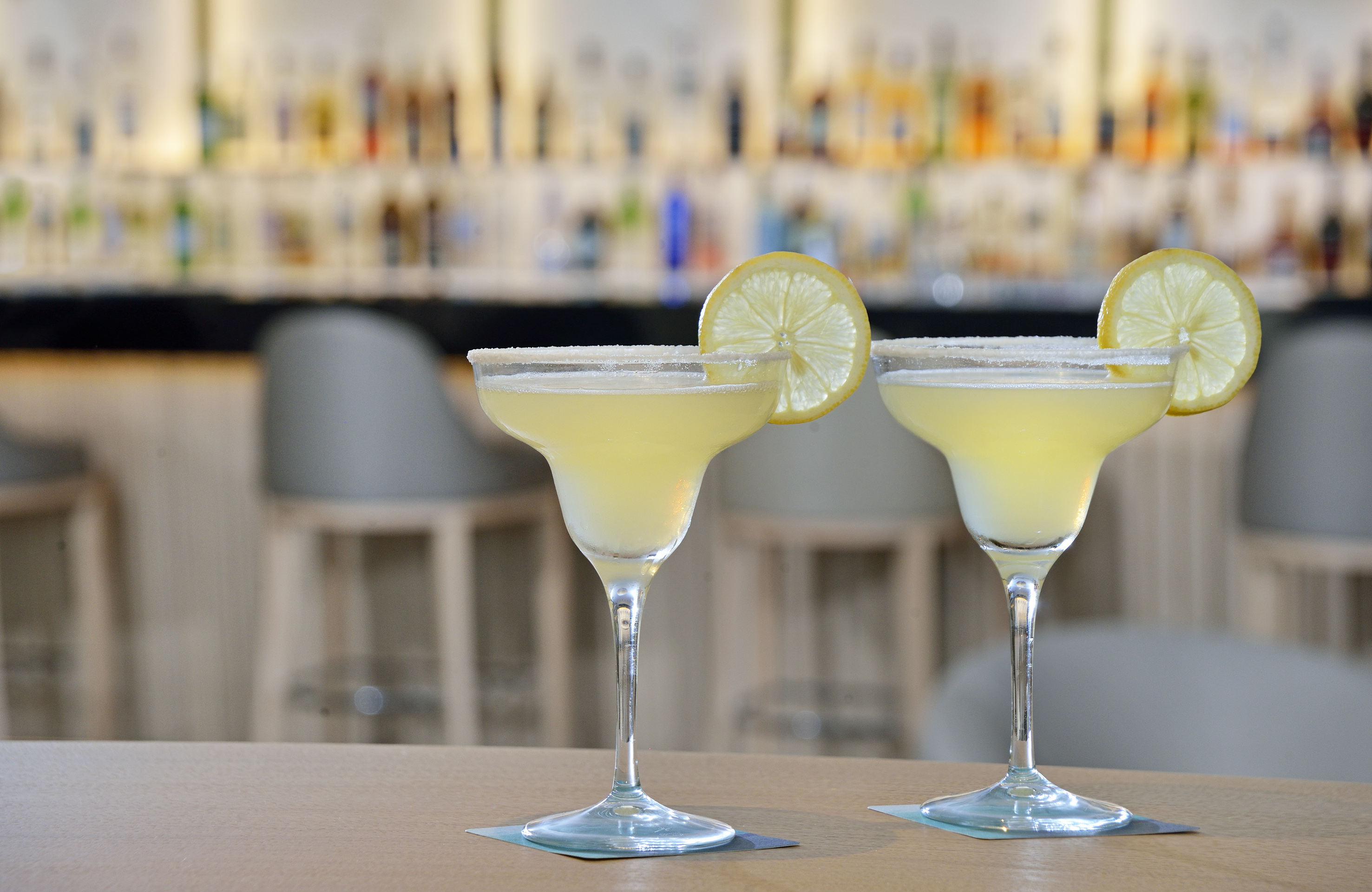 Two lemon margaritas with salt rims at a bar.