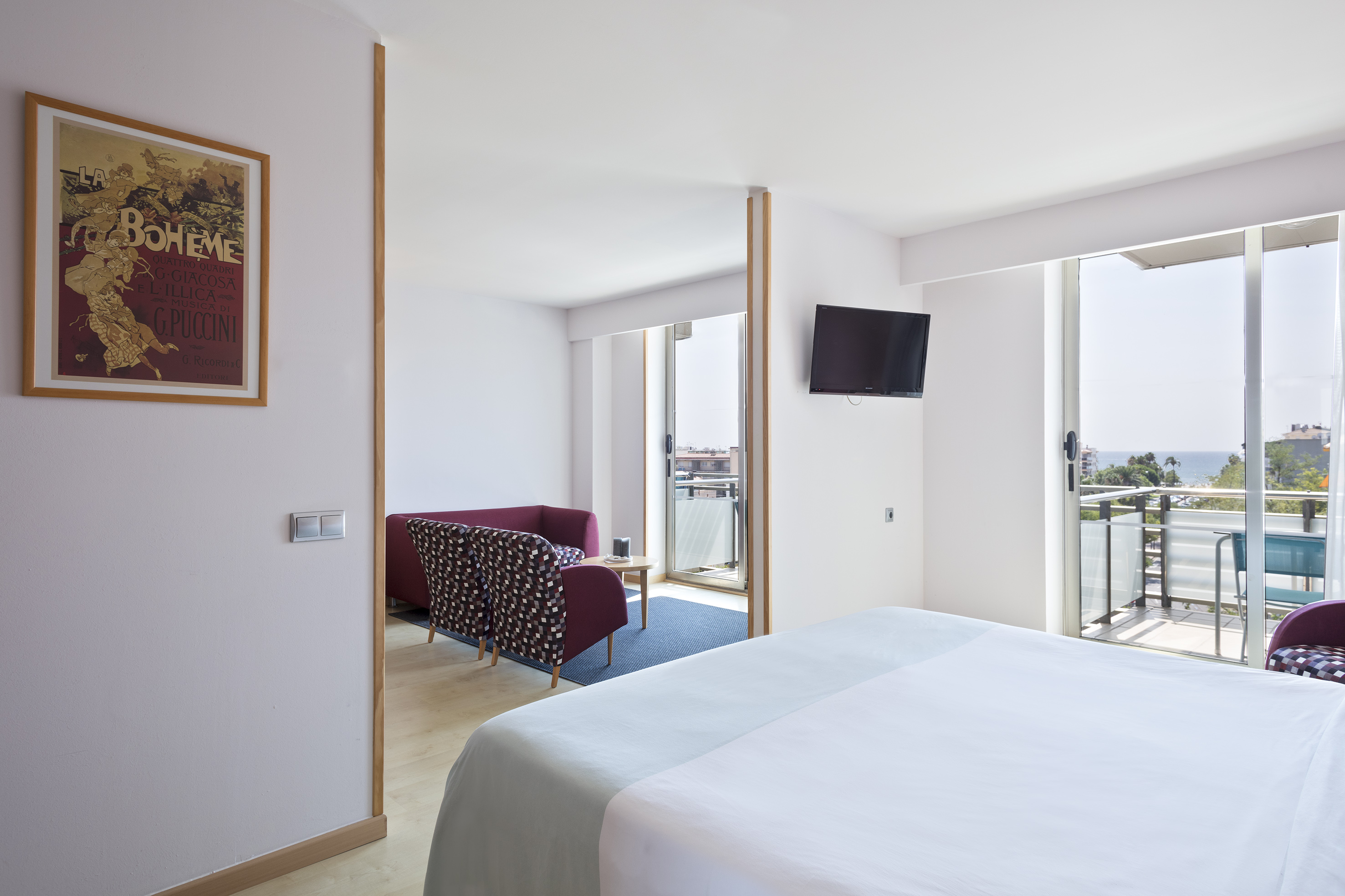 Modern hotel bedroom, separate living area, balcony with ocean view.