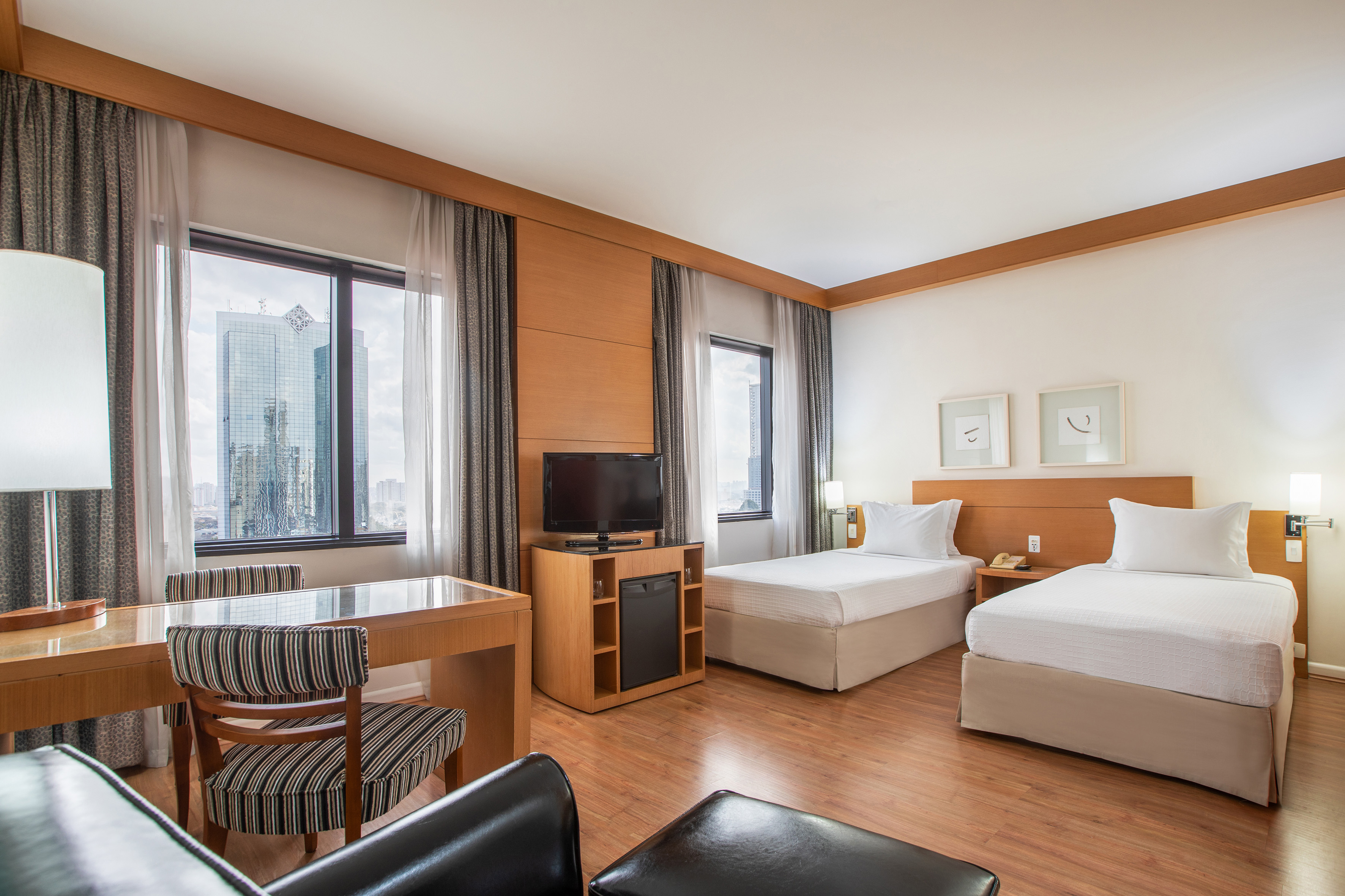 Modern hotel room with two twin beds, city view, desk, and flat-screen TV.
