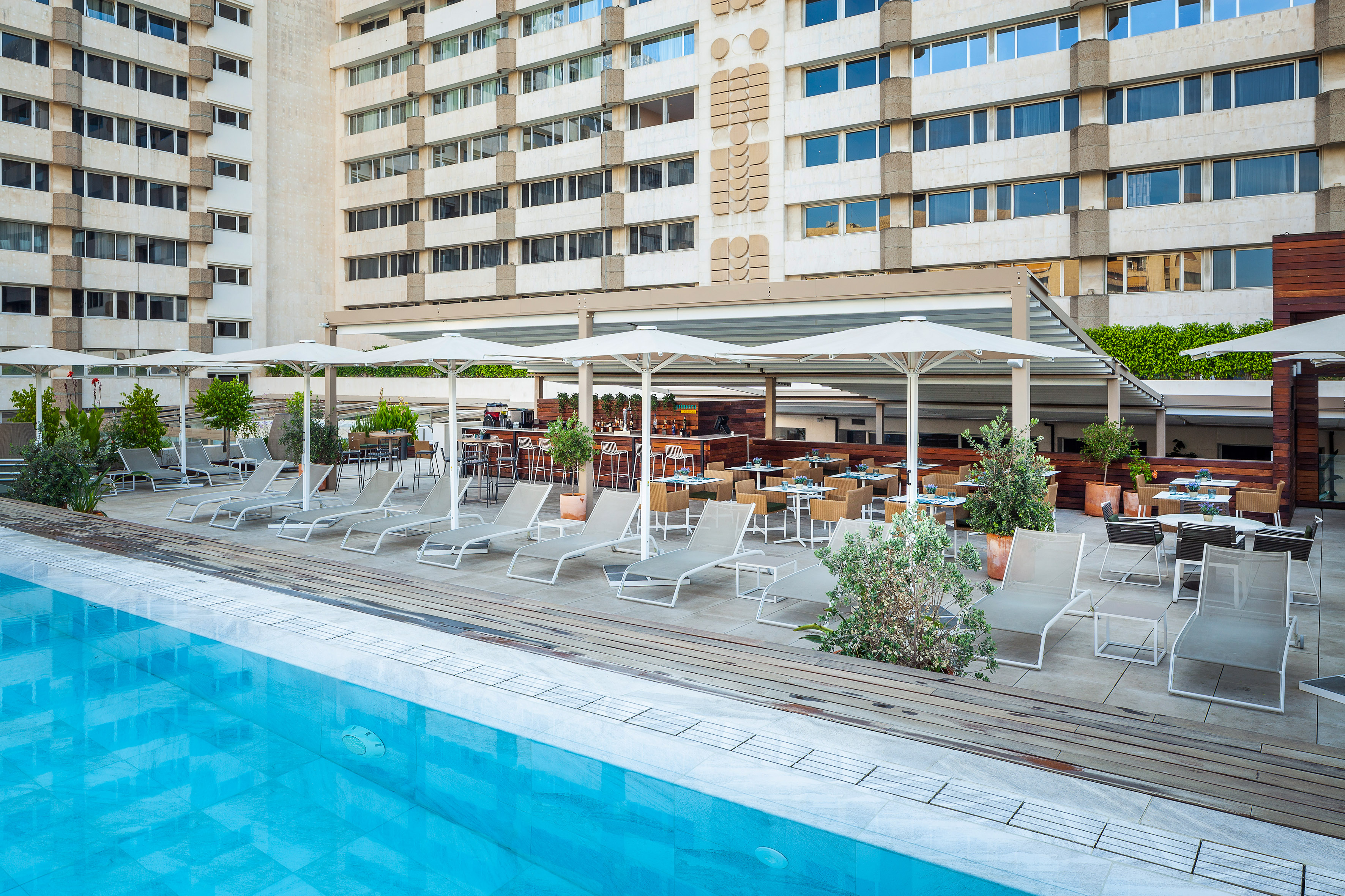 Outdoor hotel pool and lounge area with bar, dining, and building facade.