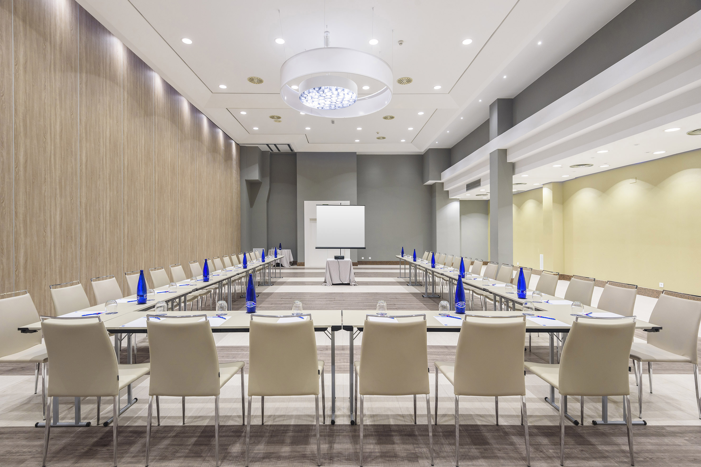 Modern conference room with U-shaped table, beige chairs, and presentation screen.