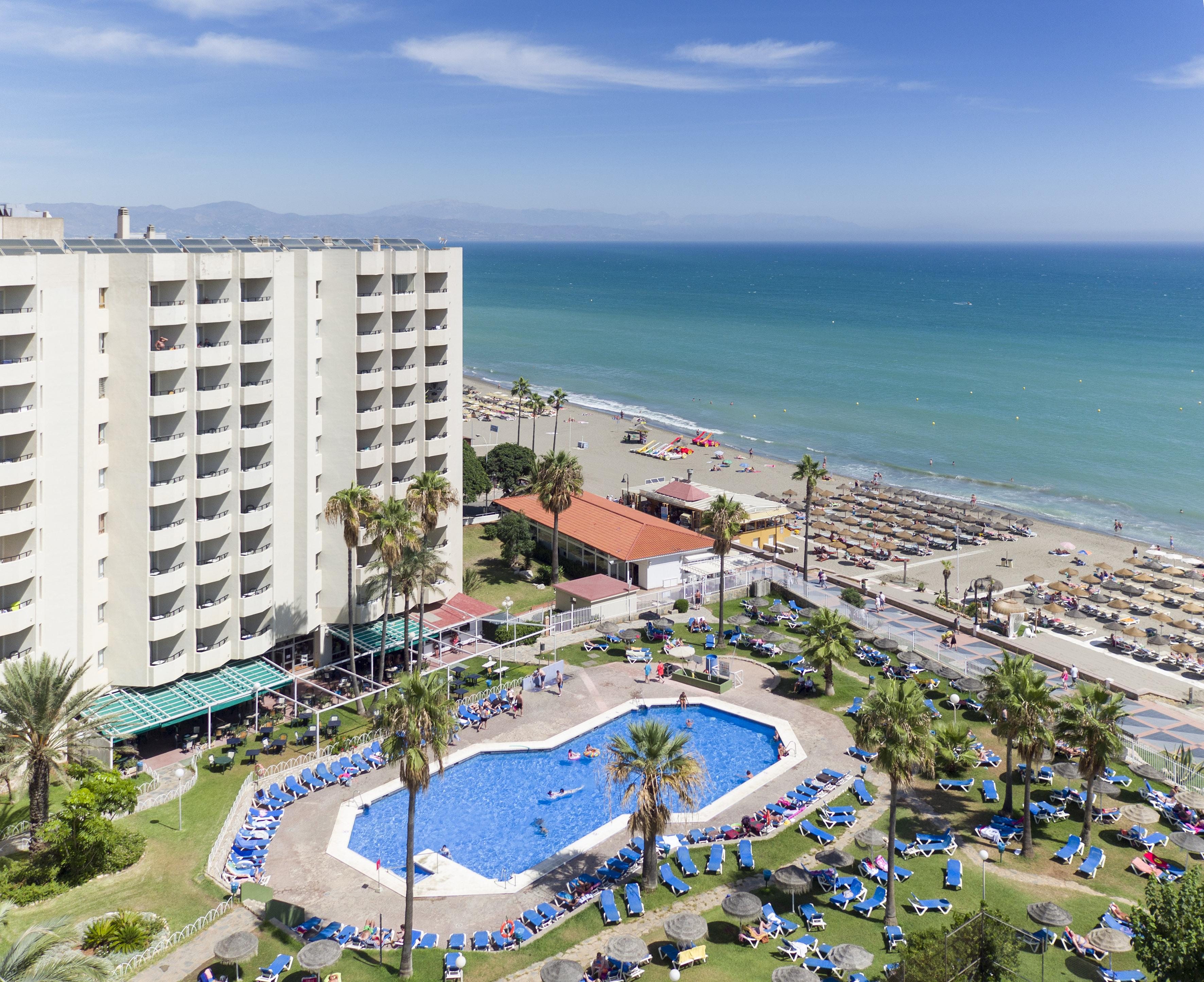 Coastal hotel resort with pool, palm trees, sandy beach, and blue ocean.