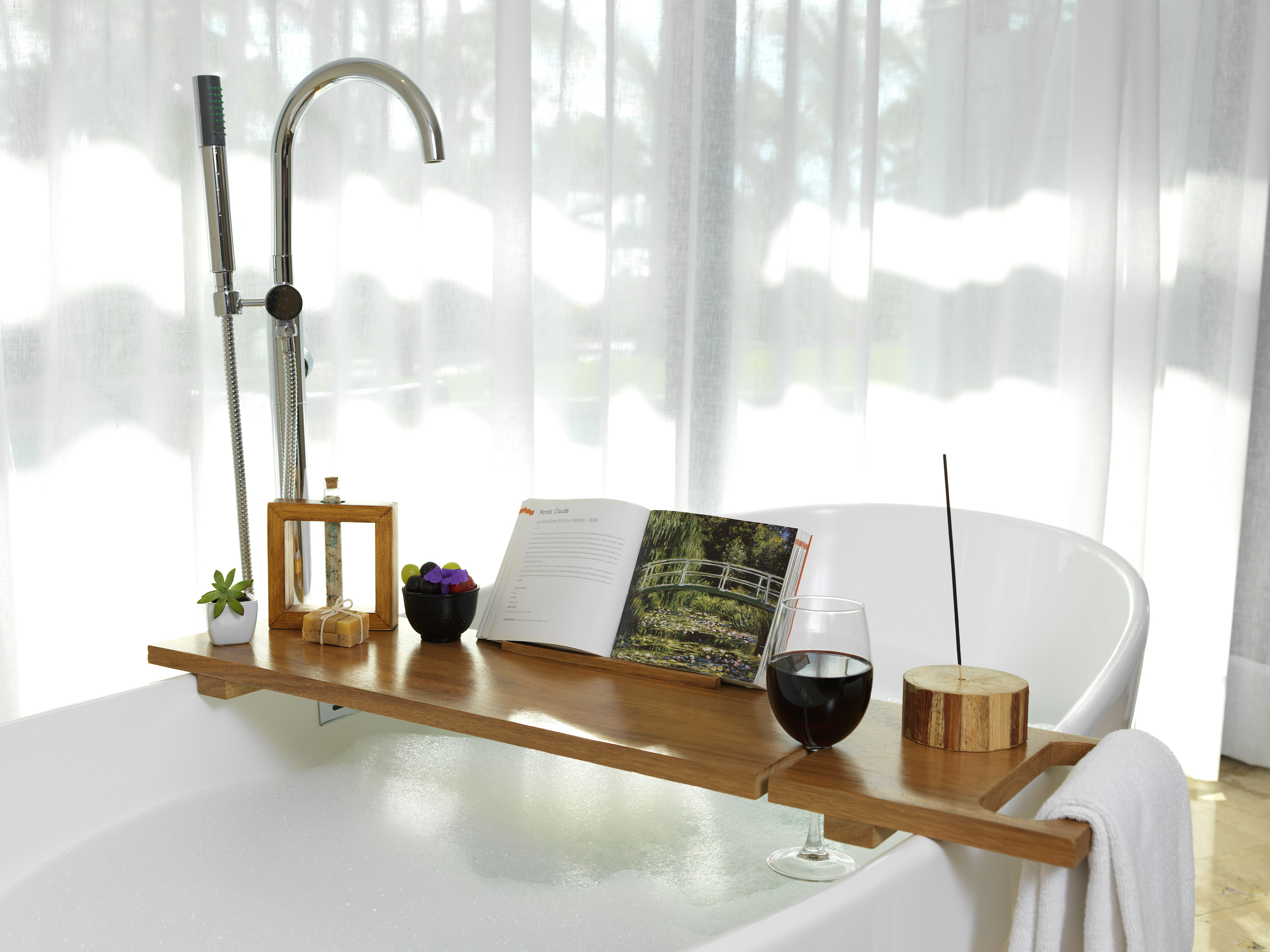 Bathtub with wooden bath caddy, open book, wine, and bath accessories.
