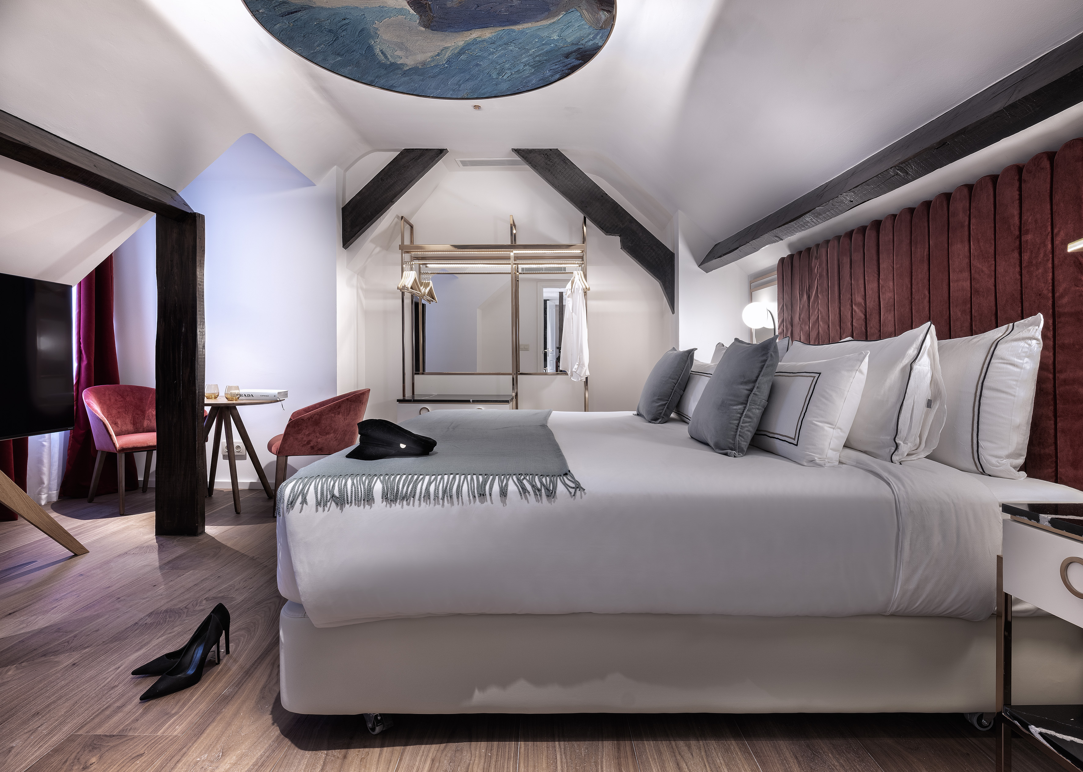 Stylish attic hotel room with king bed, red headboard, and wood beams.