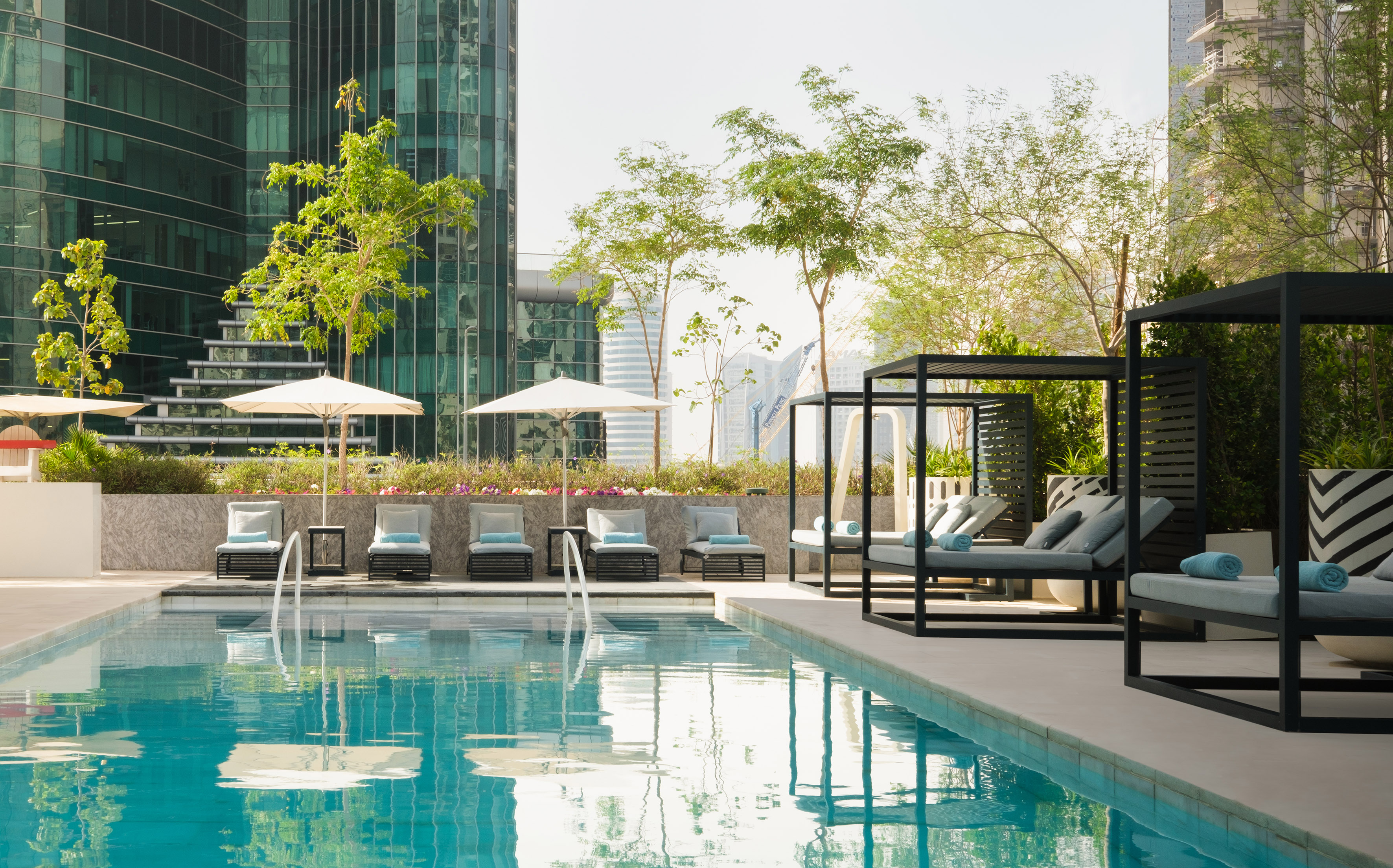 Outdoor pool with sun loungers, cabanas, umbrellas, and city skyline.