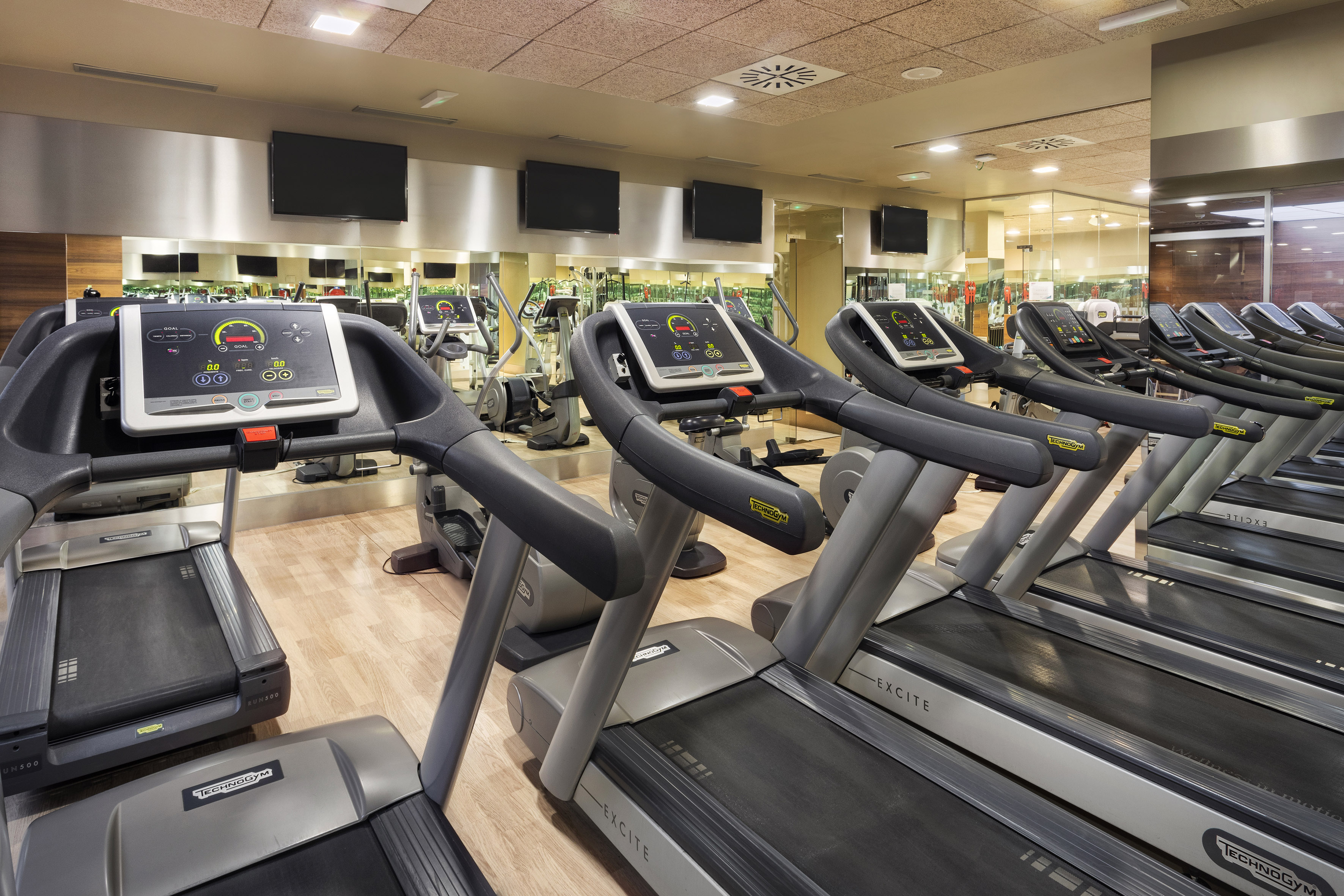 Row of Technogym treadmills in a modern gym with screens and mirrors.