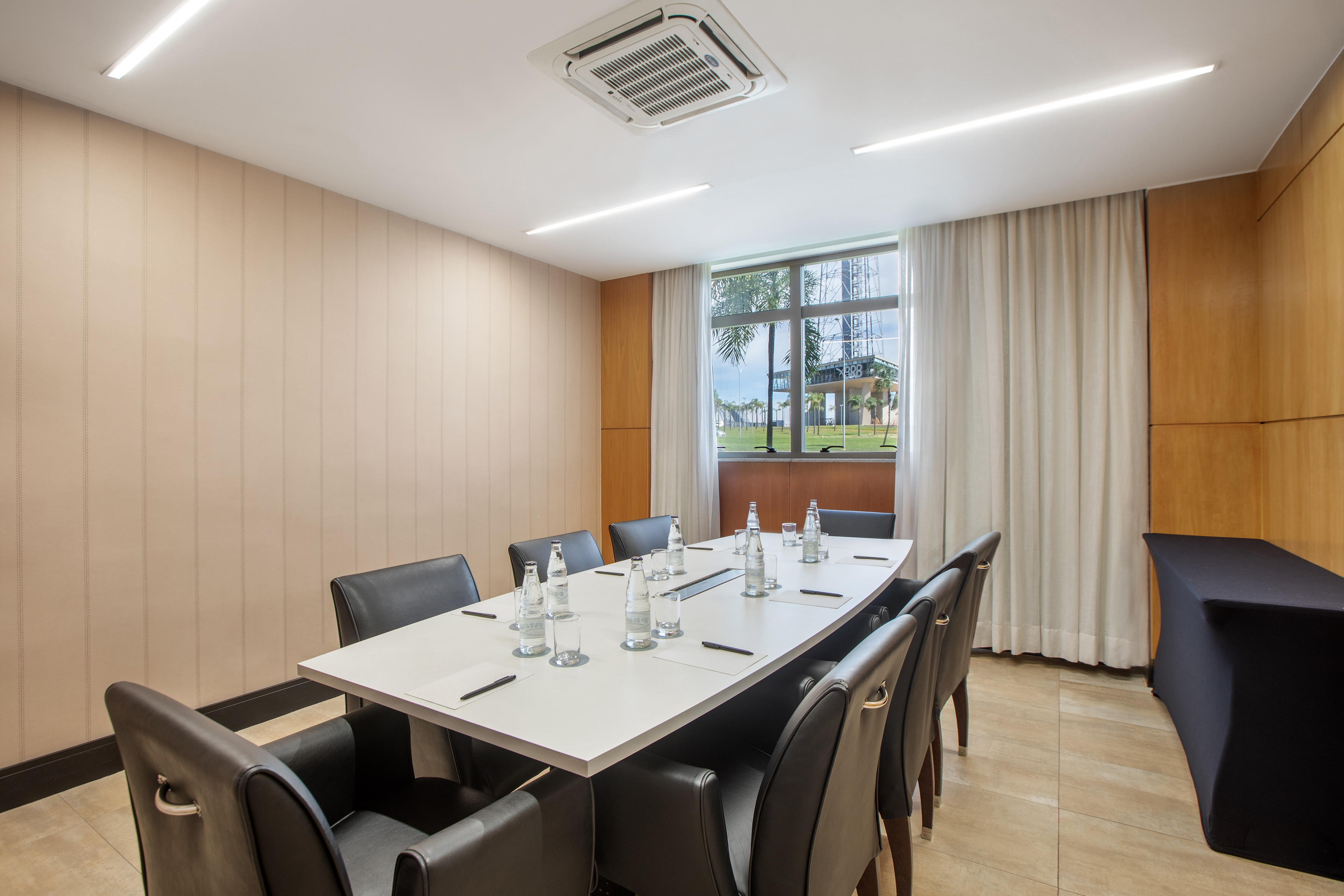 Modern conference room with white table, black leather chairs, and window view.