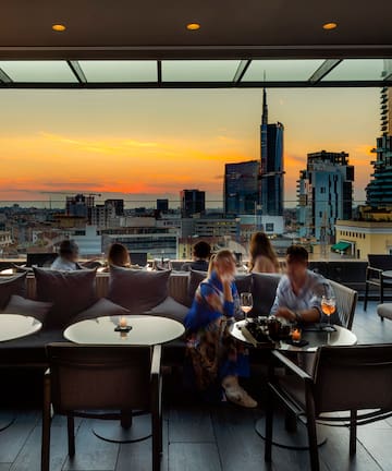 a group of people sitting at tables and chairs in a rooftop bar