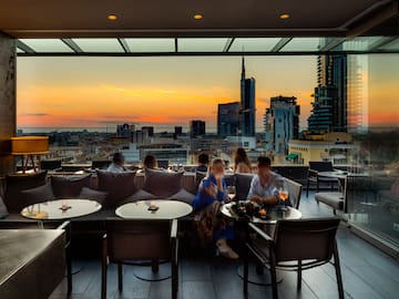 a group of people sitting at tables and chairs in a rooftop bar