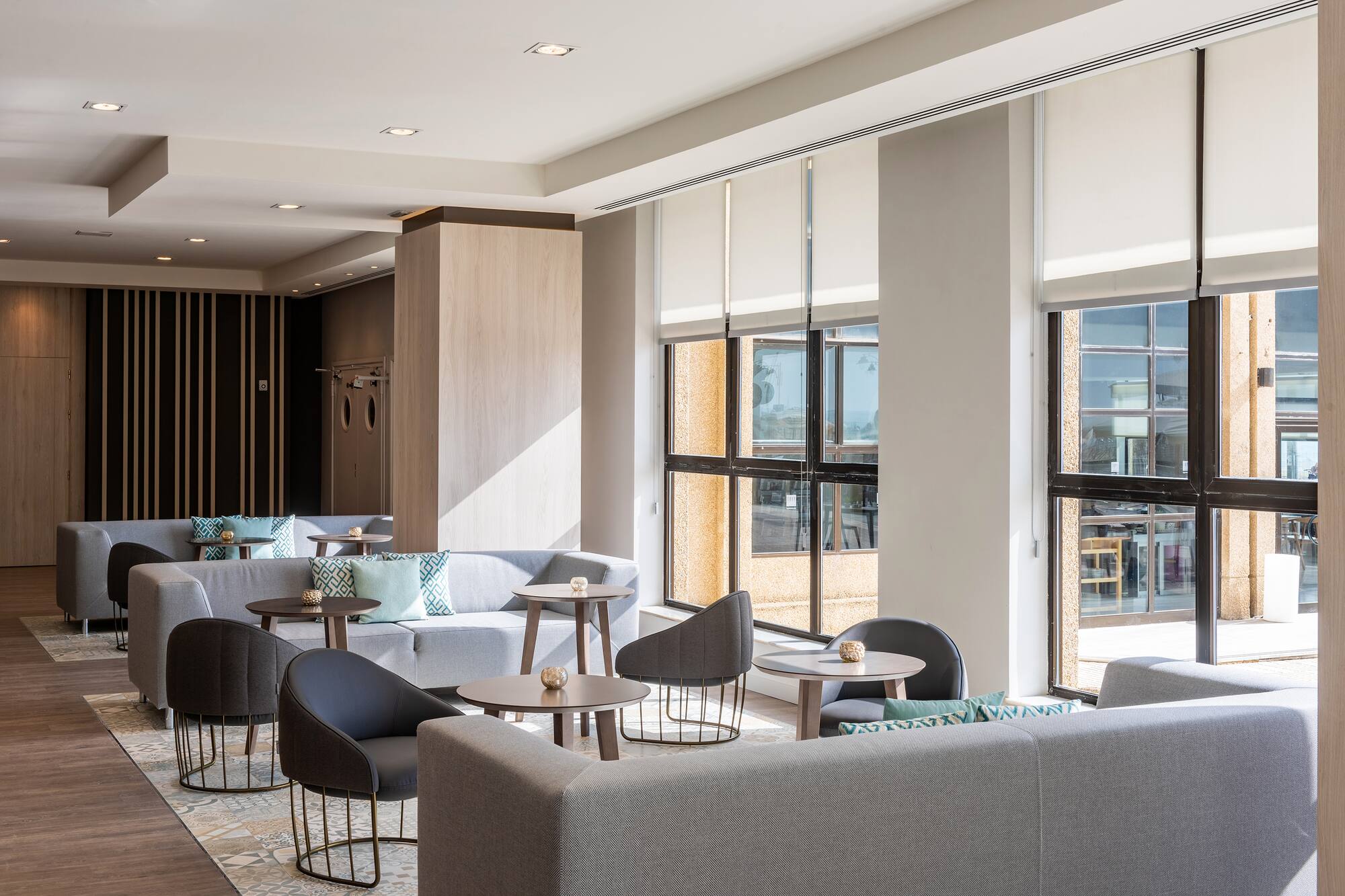 Bright modern hotel lounge with comfortable grey seating and large windows.
