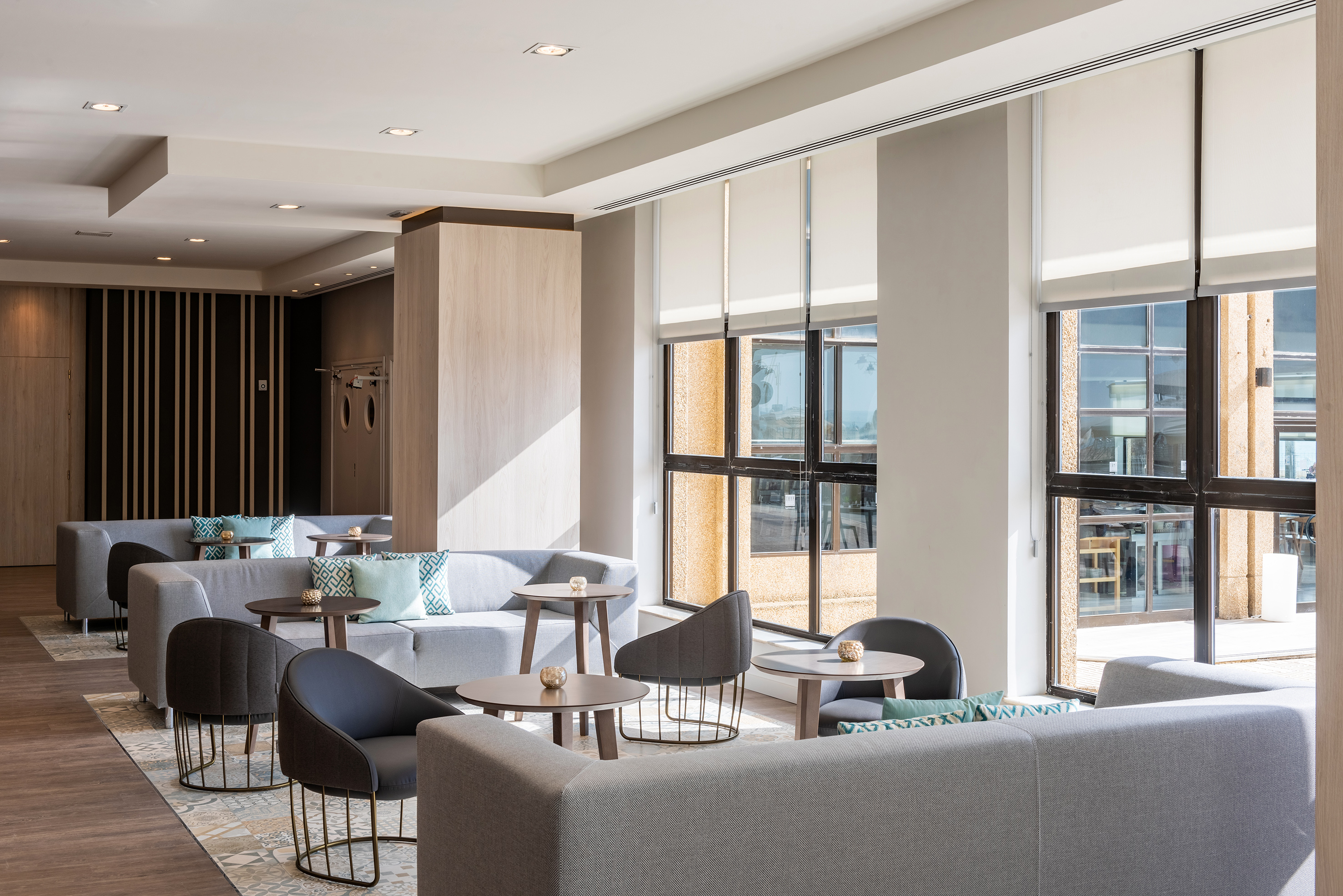 Bright modern hotel lounge with comfortable grey seating and large windows.