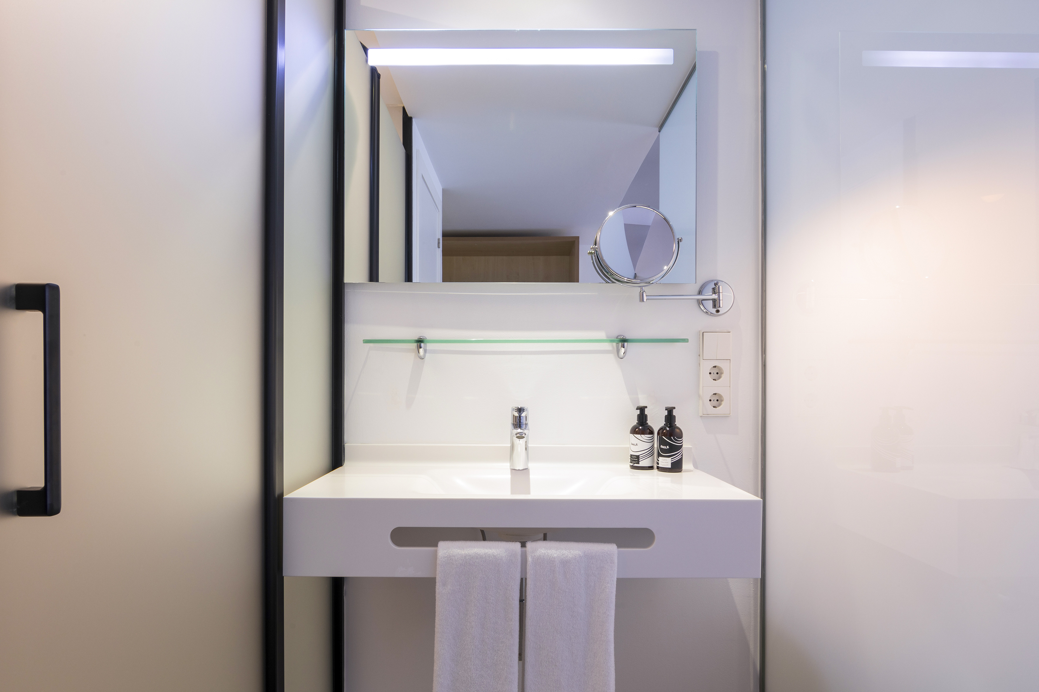 Modern hotel bathroom vanity: white sink, illuminated mirror, and towels.