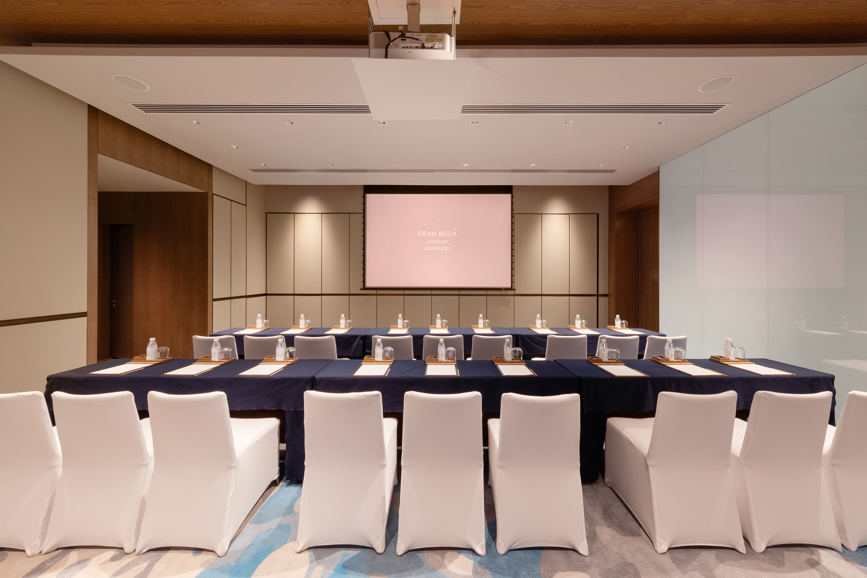 Gran Meliá Chengdu meeting room, dark blue tables, white chairs, projector screen.