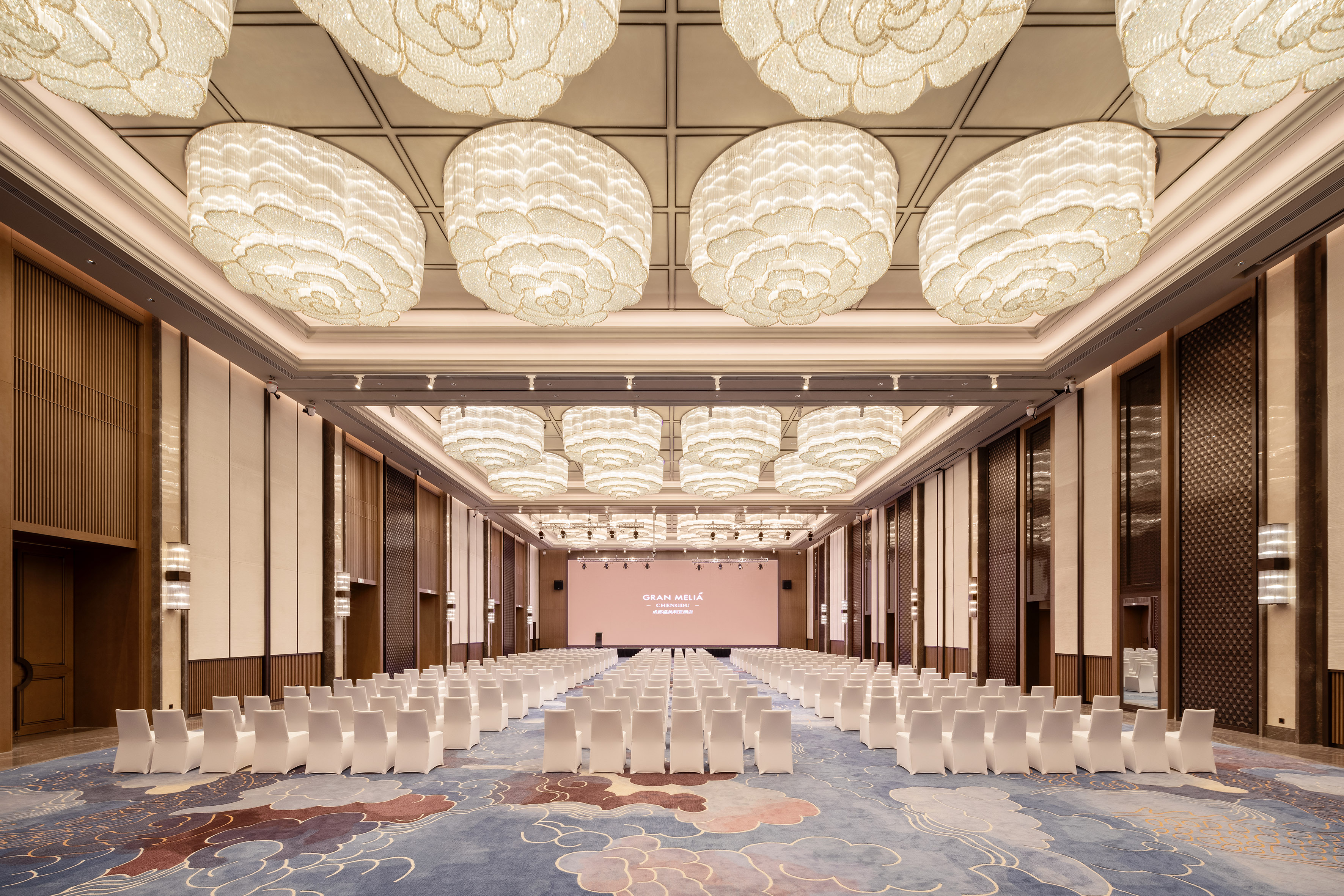 Spacious Gran Meliá Chengdu ballroom, elegant chandeliers, rows of white chairs.