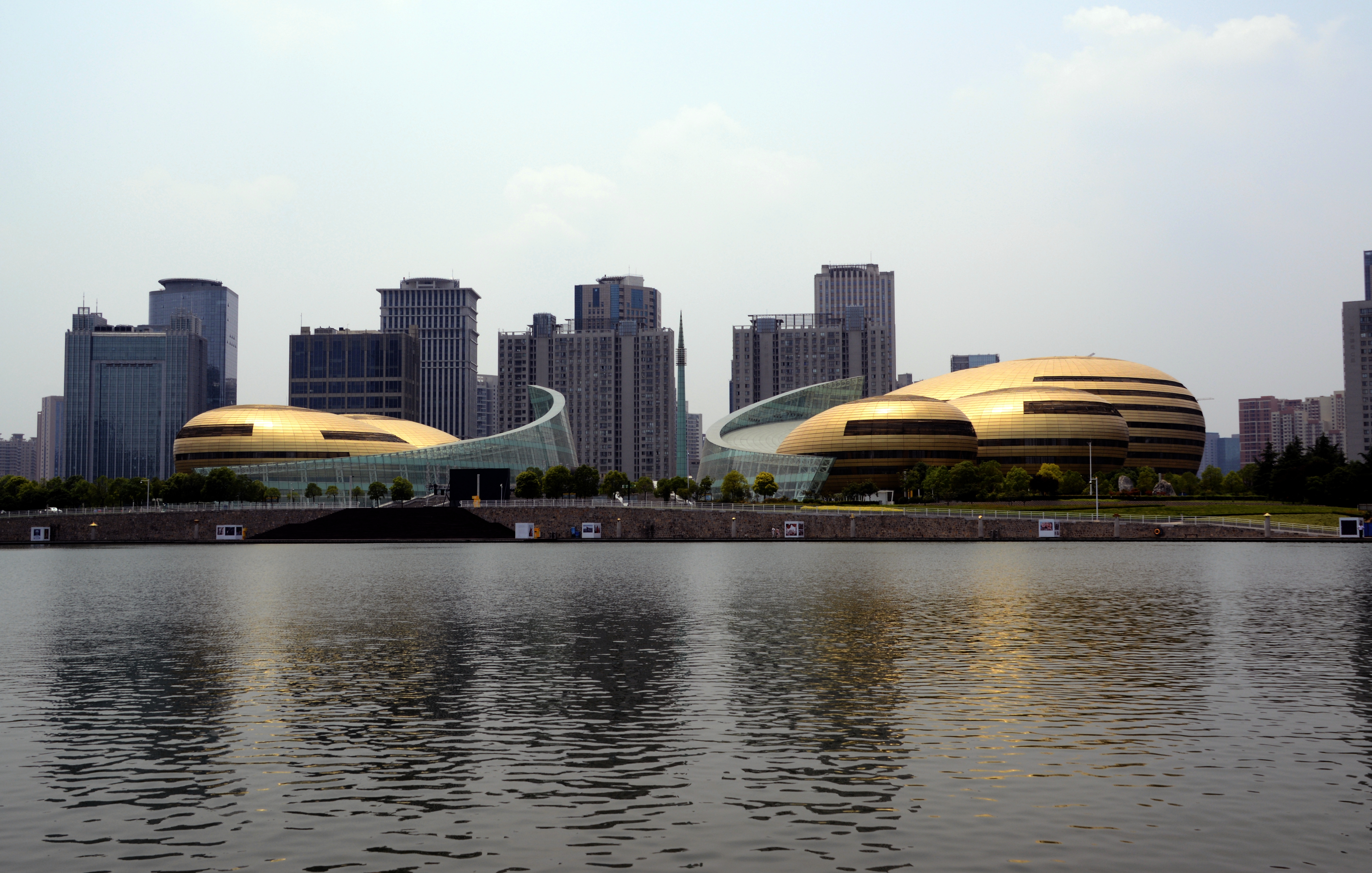 Modern golden buildings, skyscrapers, and glass structures by a city river.