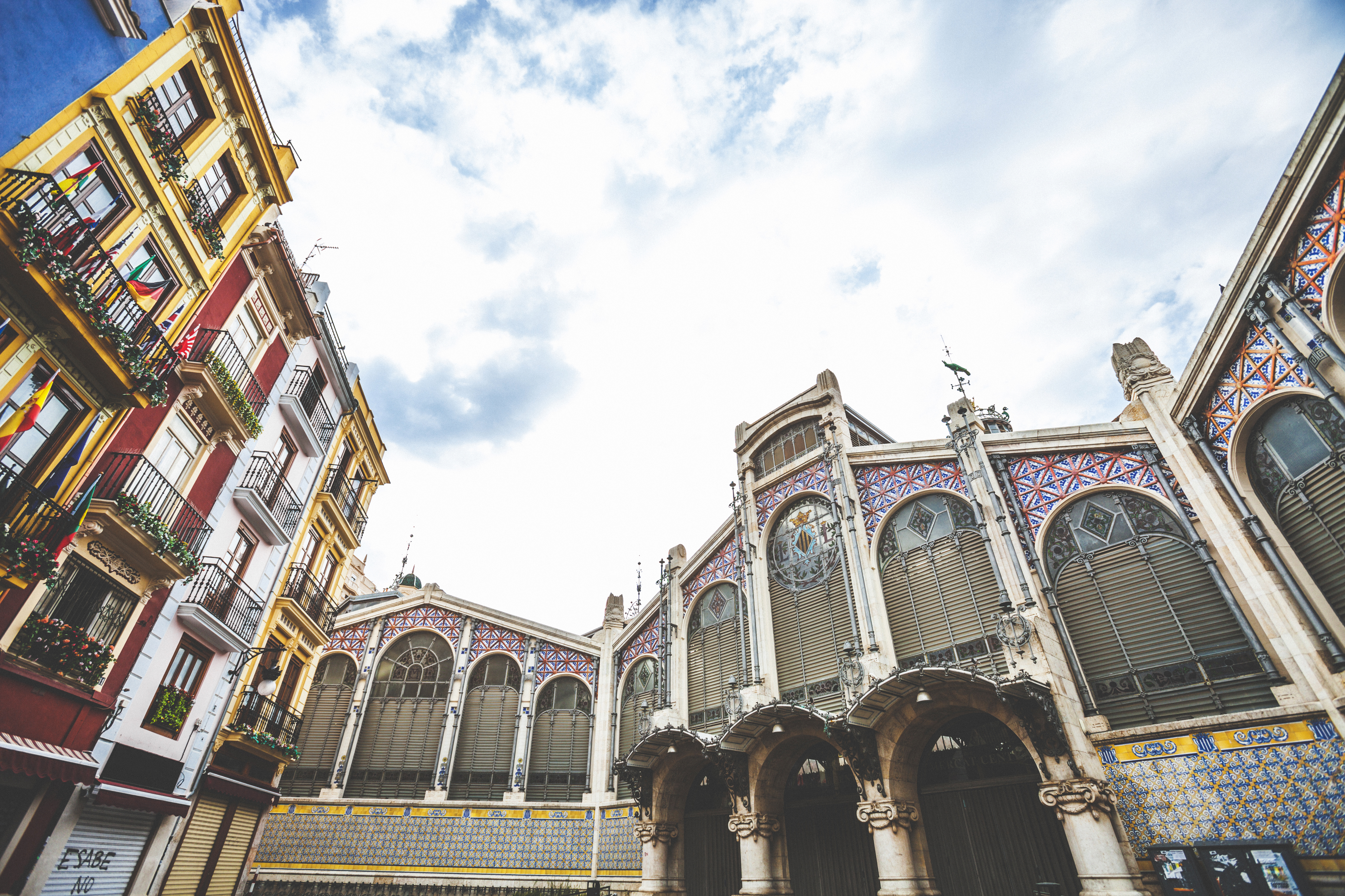 Ornate Valencia Central Market architecture next to colorful city buildings under cloudy sky.