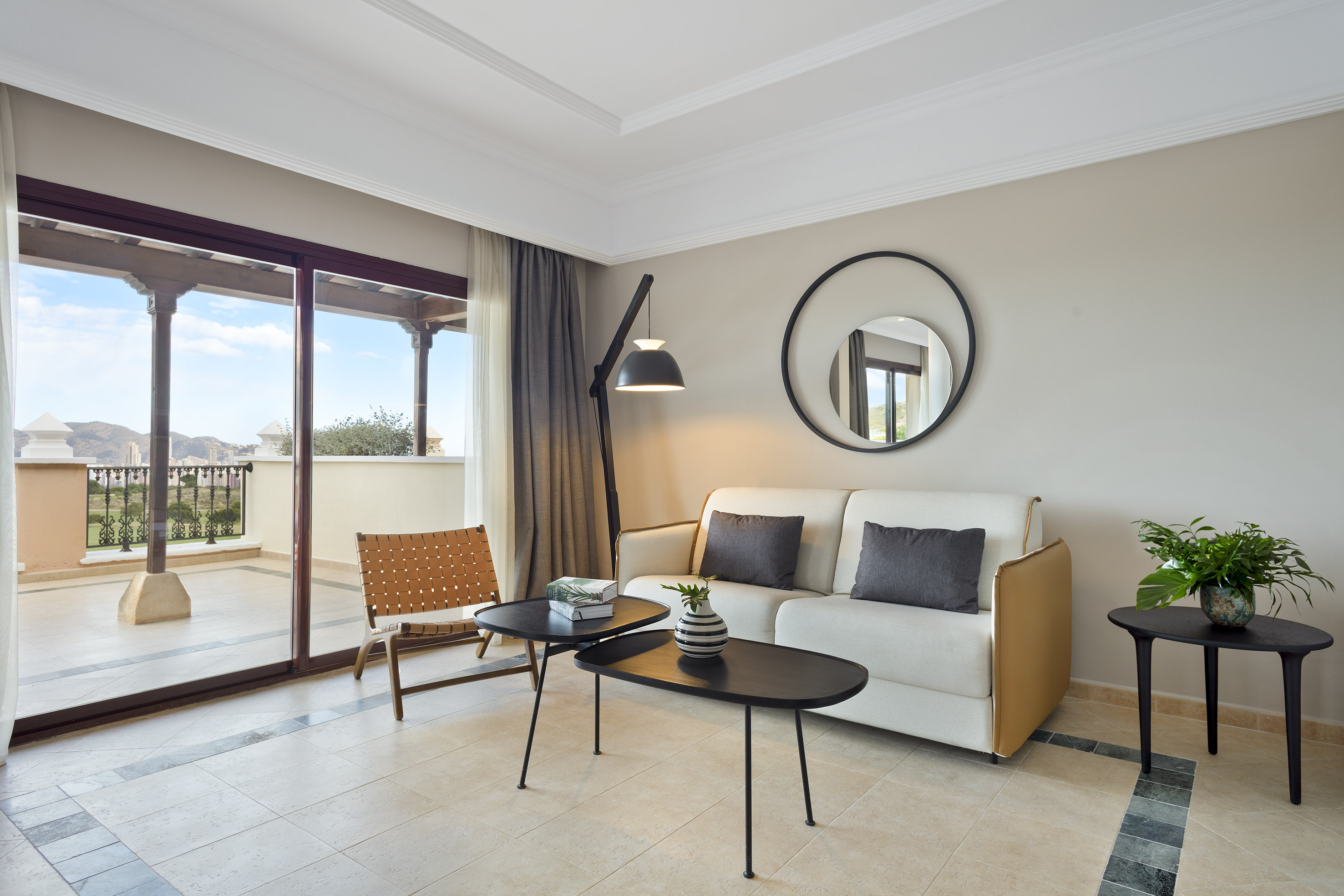Modern living room with sofa, black tables, and balcony overlooking mountains.