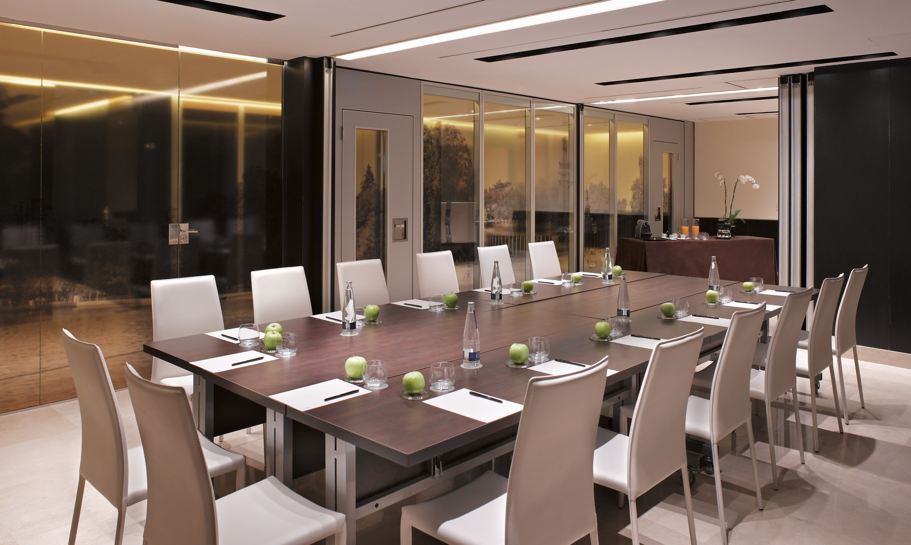 Modern conference room with large table, white chairs, water, and fresh apples.