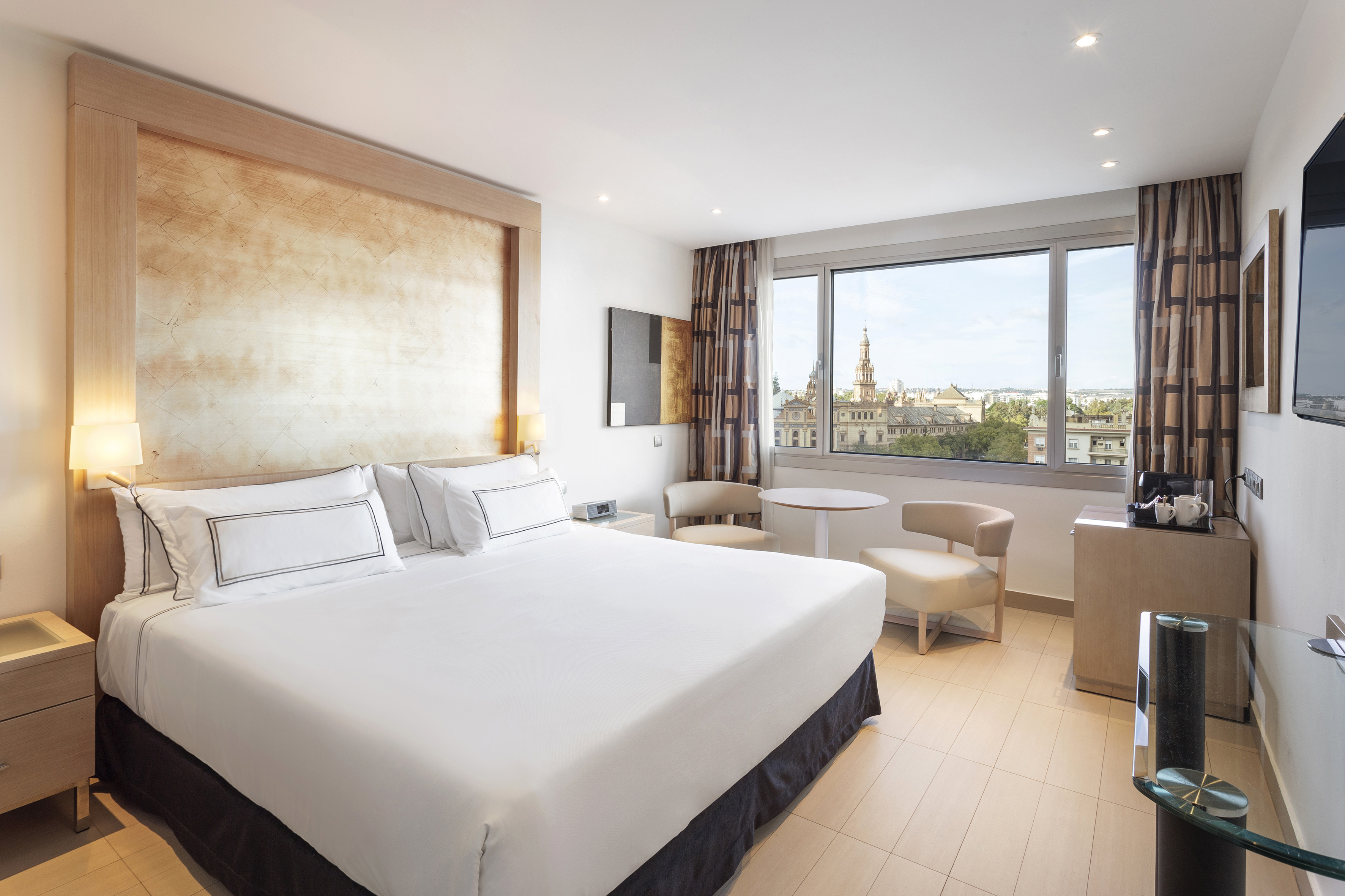 Stylish hotel room with large bed, modern decor, and panoramic city view.
