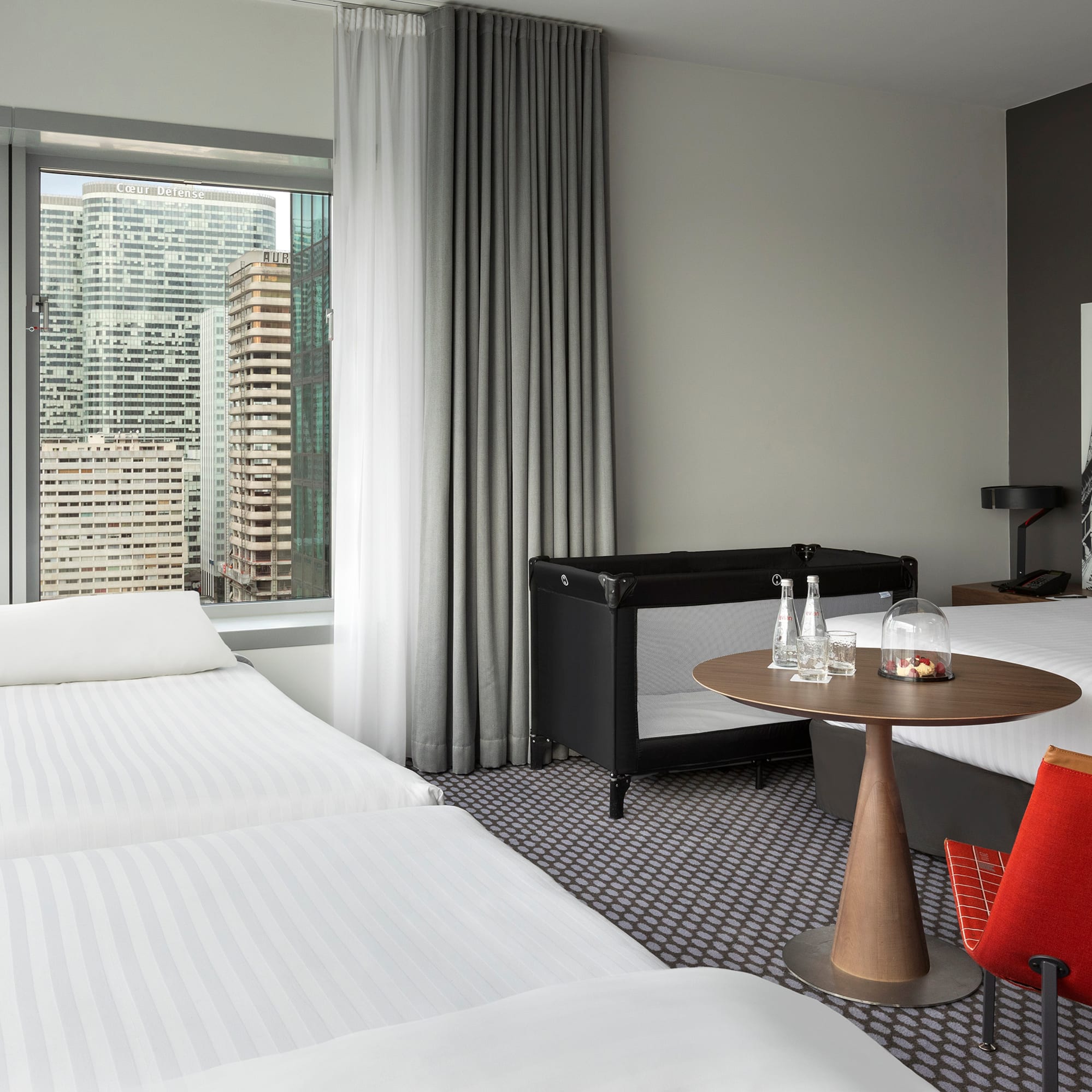 Family hotel room with Paris city view, Grande Arche, and baby crib.