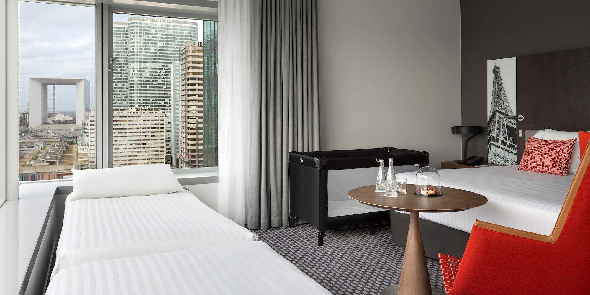 Family hotel room with Paris city view, Grande Arche, and baby crib.