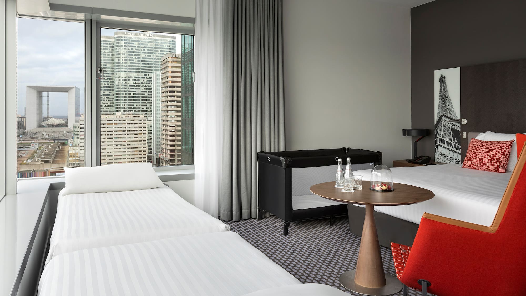 Family hotel room with Paris city view, Grande Arche, and baby crib.
