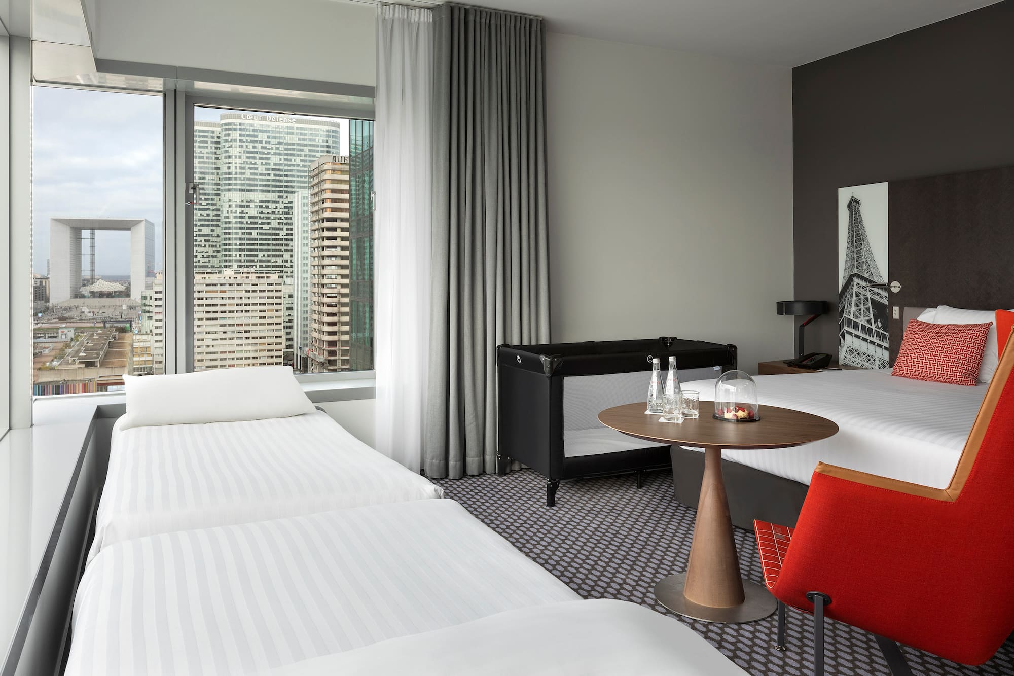 Family hotel room with Paris city view, Grande Arche, and baby crib.