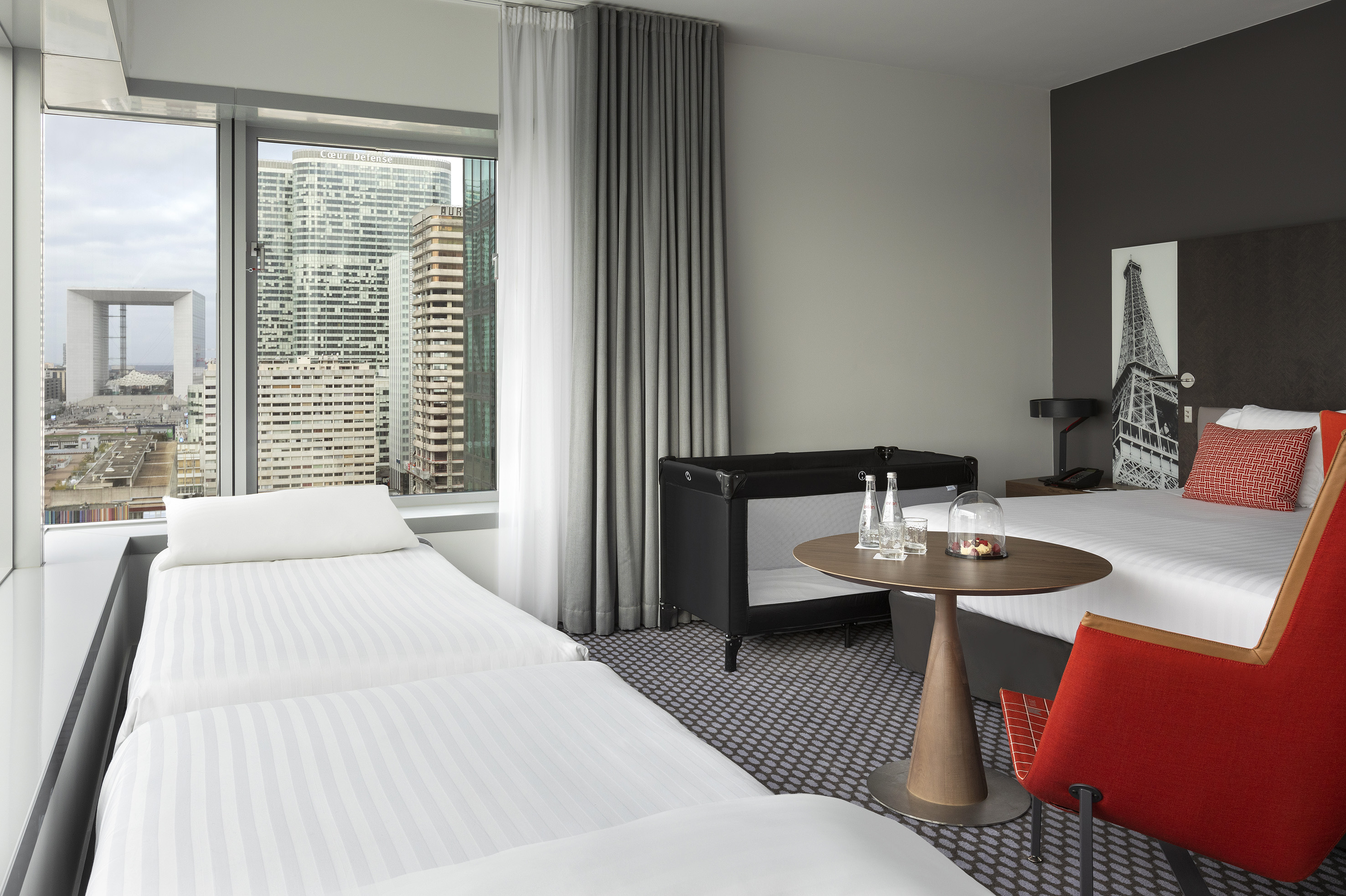 Family hotel room with Paris city view, Grande Arche, and baby crib.