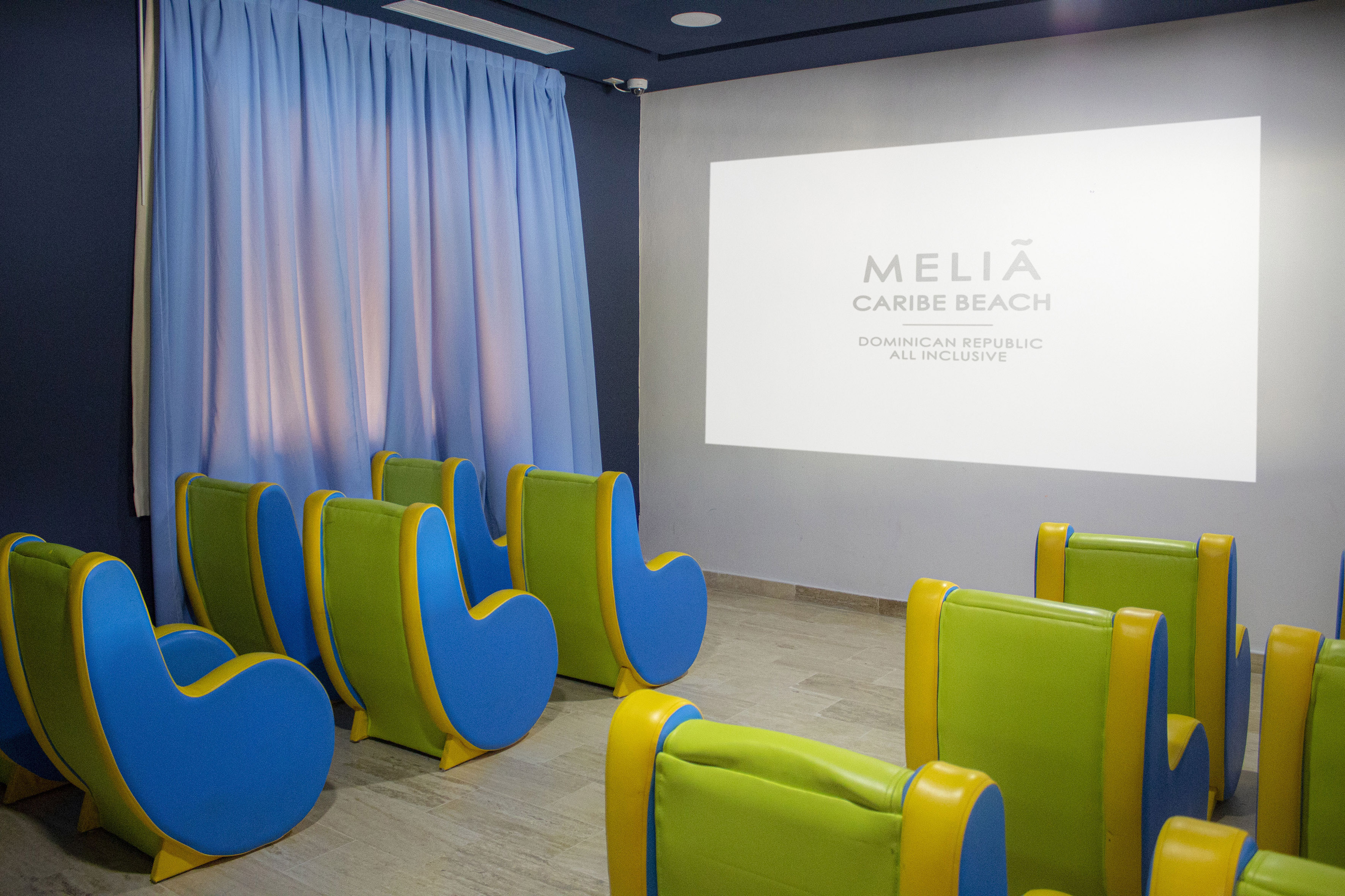 Kids cinema room with Meliã Caribe Beach logo on screen and colorful seats.