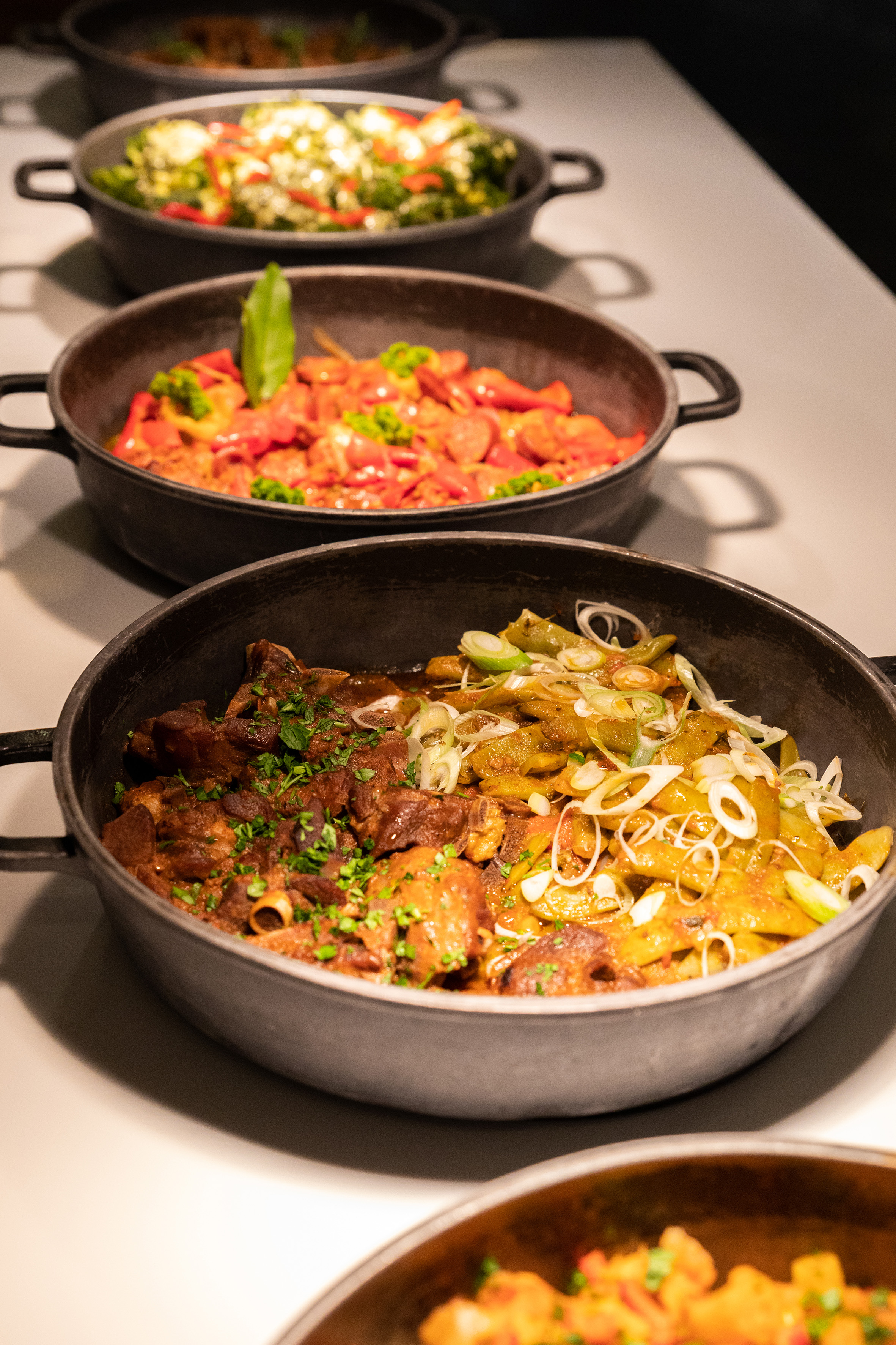 Hot buffet in black pots: meat stew, seasoned vegetables, and pepper dish.