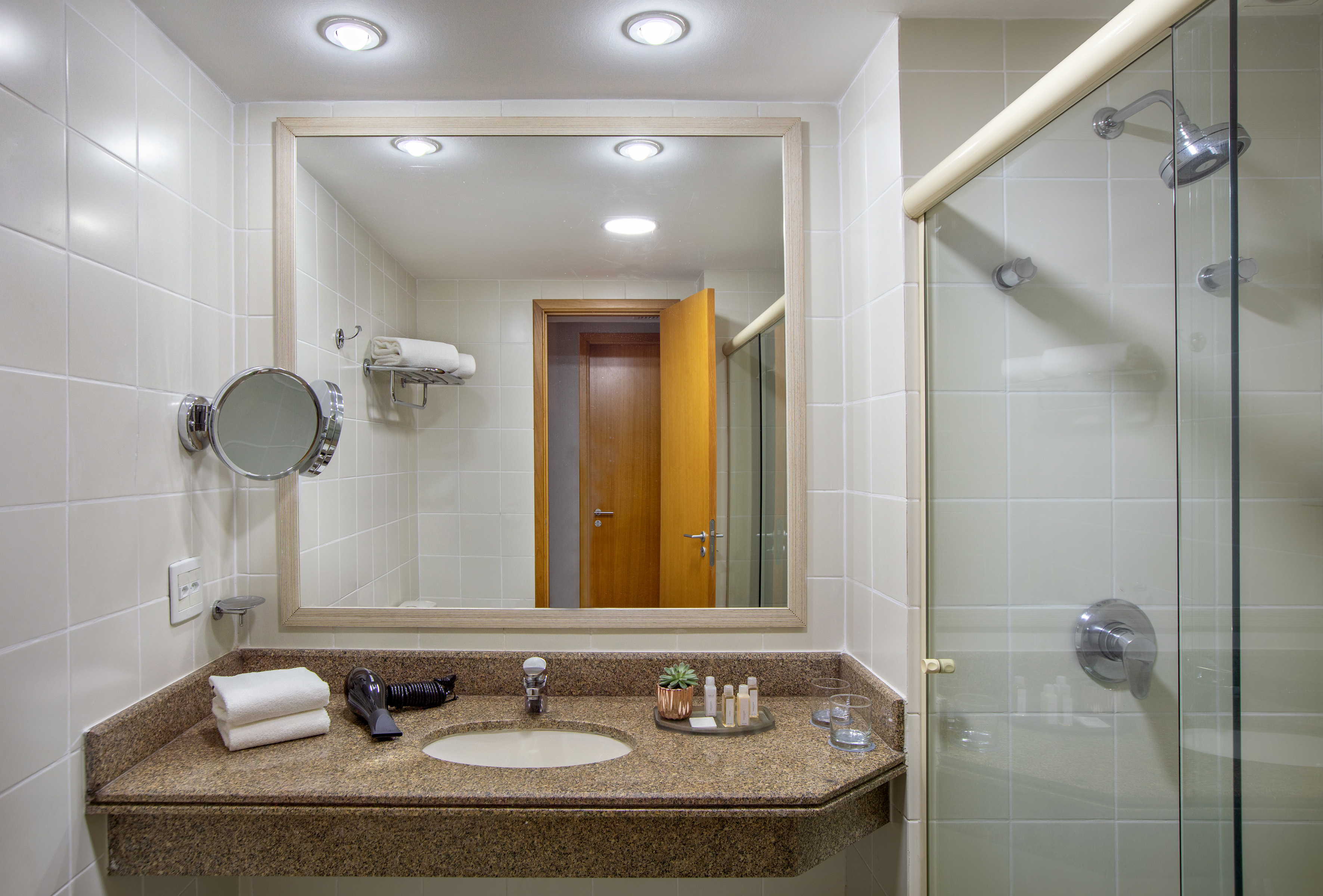 Modern hotel bathroom vanity, large mirror, granite counter, glass shower.