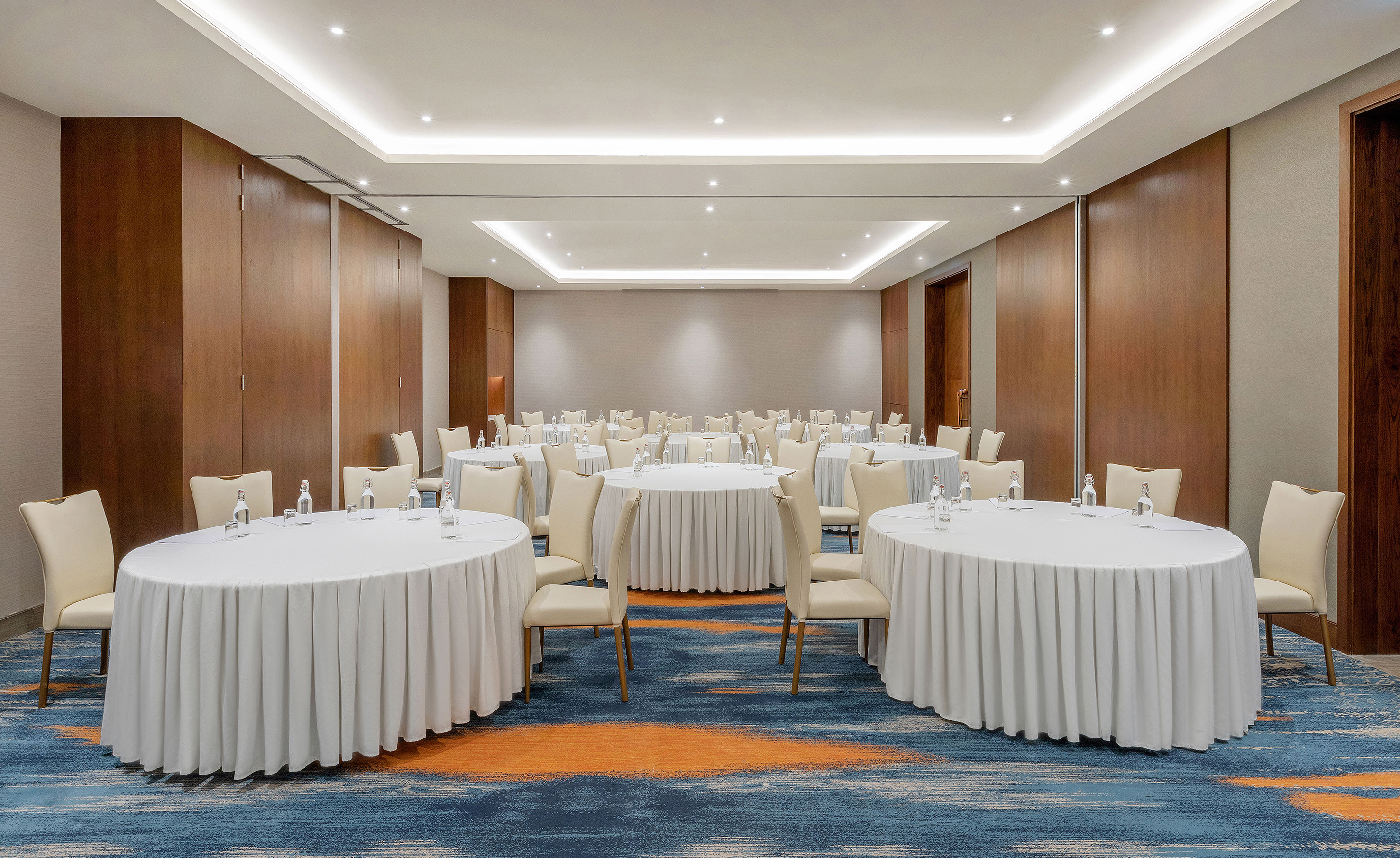 Event hall with round tables, cream chairs, and blue patterned carpet.