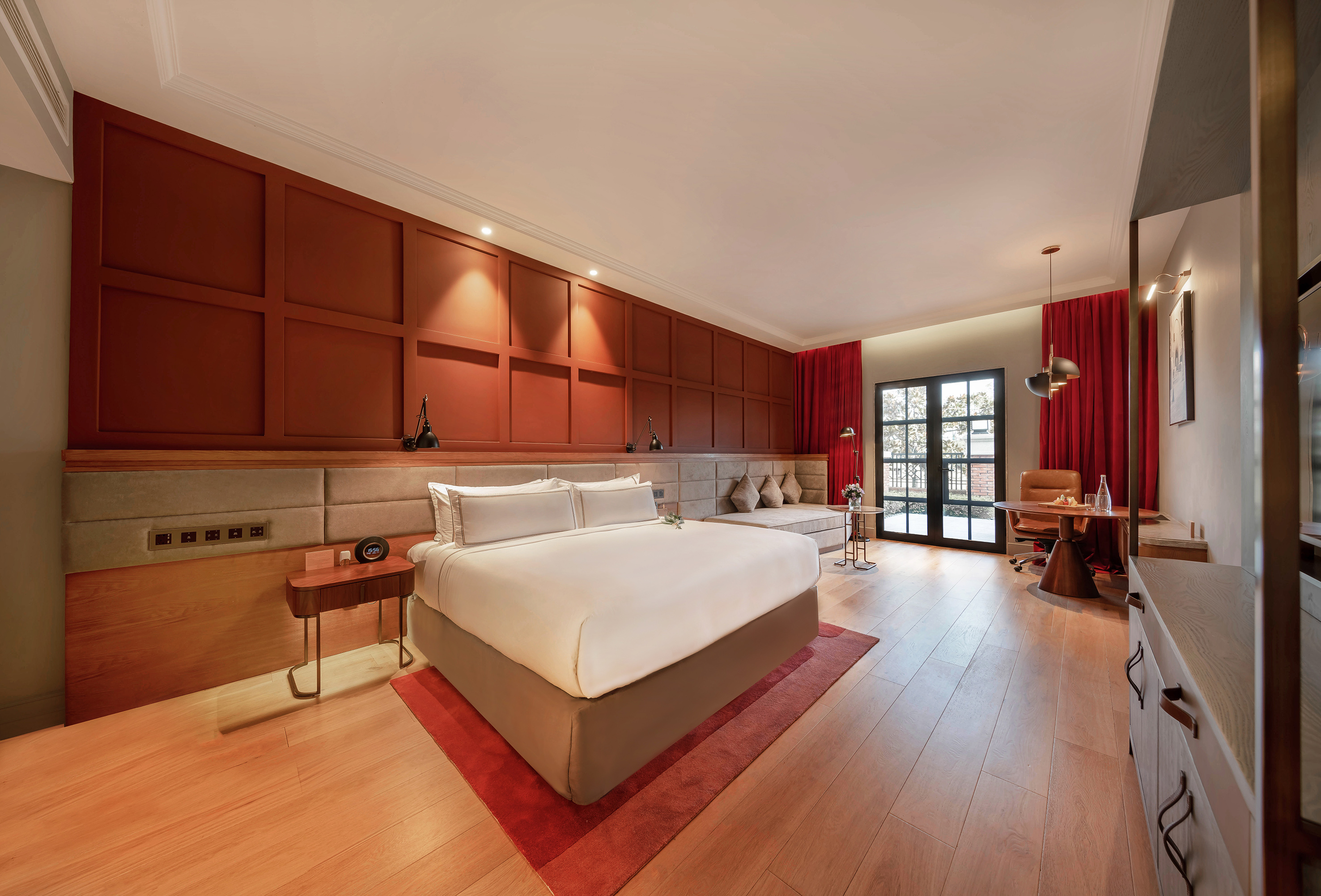 Modern hotel bedroom with large bed, red paneled wall, and balcony access.
