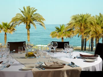 a table set for a dinner with palm trees and water in the background