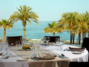 a table set for a dinner with palm trees and water in the background