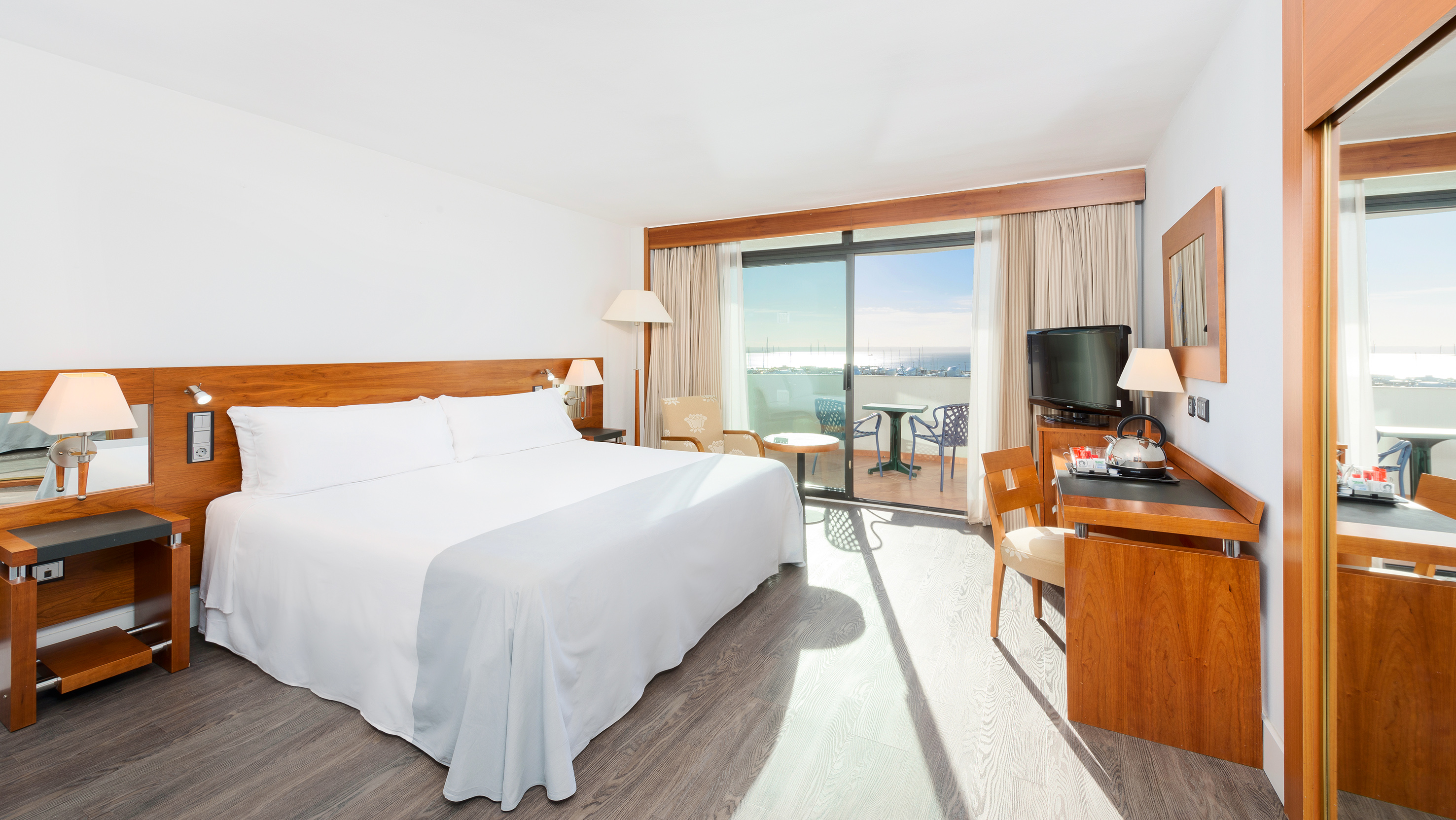 Bright hotel bedroom with white bed and balcony overlooking a marina.
